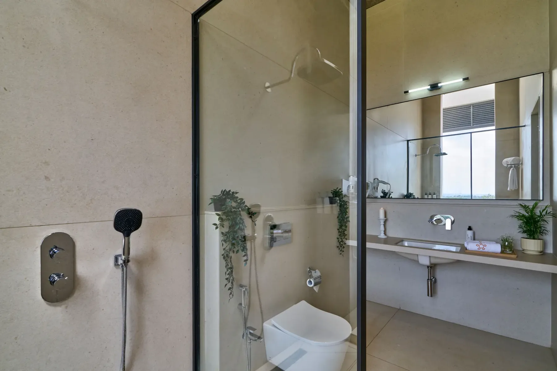 Un baño moderno con ducha de vidrio, inodoro y lavabo bajo un espejo amplio.