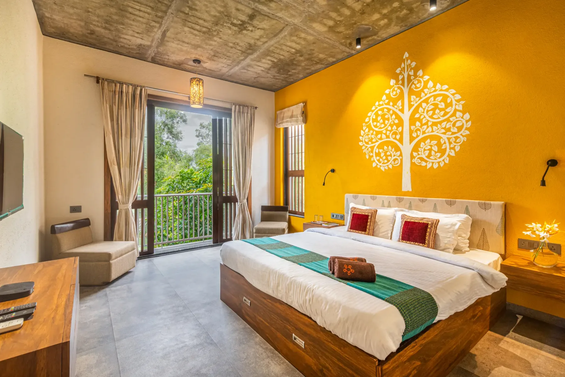 A bedroom with a large bed facing a yellow wall decorated with a tree design.