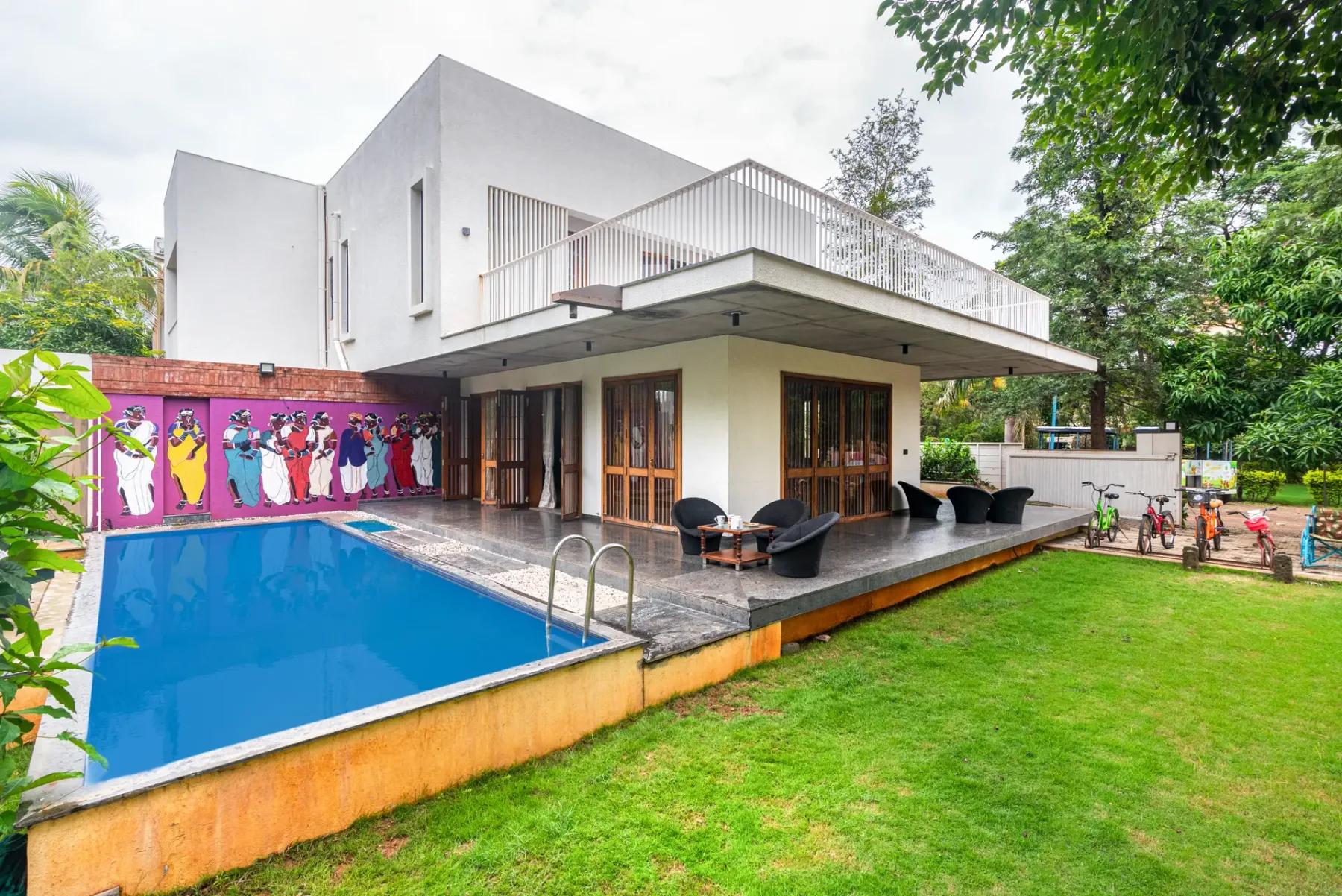 A modern house opens onto a poolside patio and green lawn.
