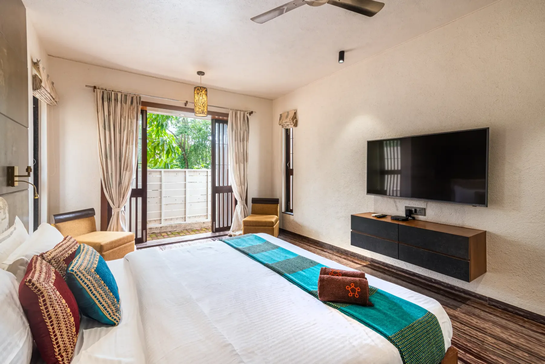 A bedroom with a large bed, a television, and glass doors opening onto greenery.