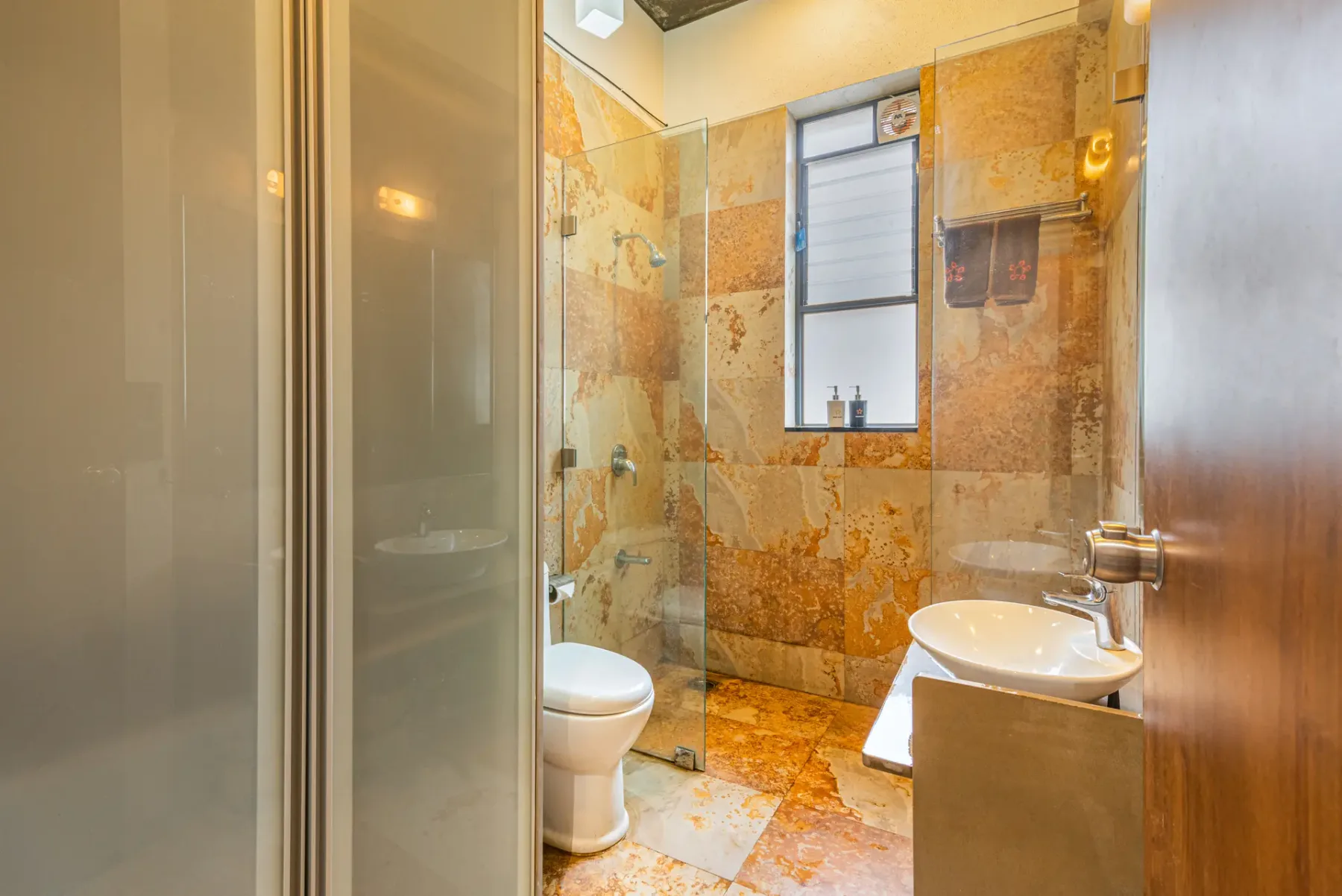 A bathroom with a glass shower, toilet, and sink.