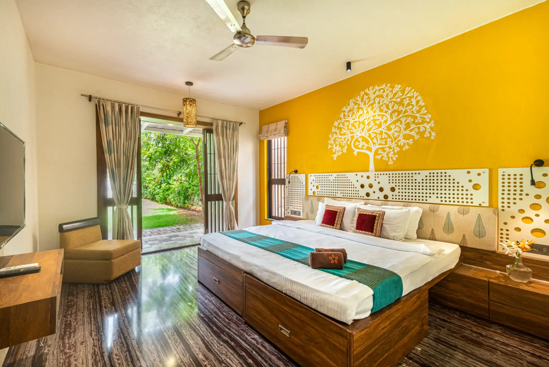 A bedroom with a wooden bed, colorful bedding, and an open glass door to greenery.