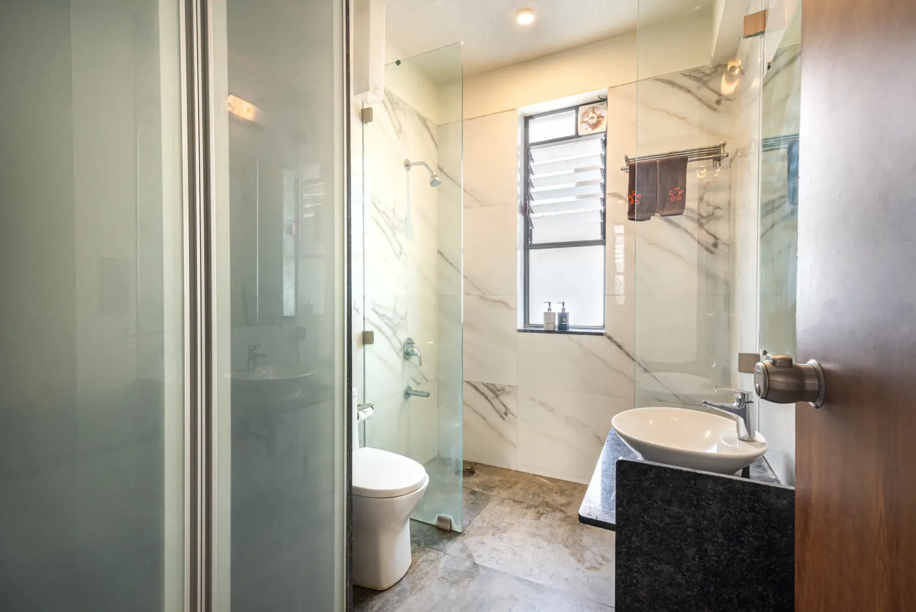 A bright bathroom with a glass shower, toilet, and basin.
