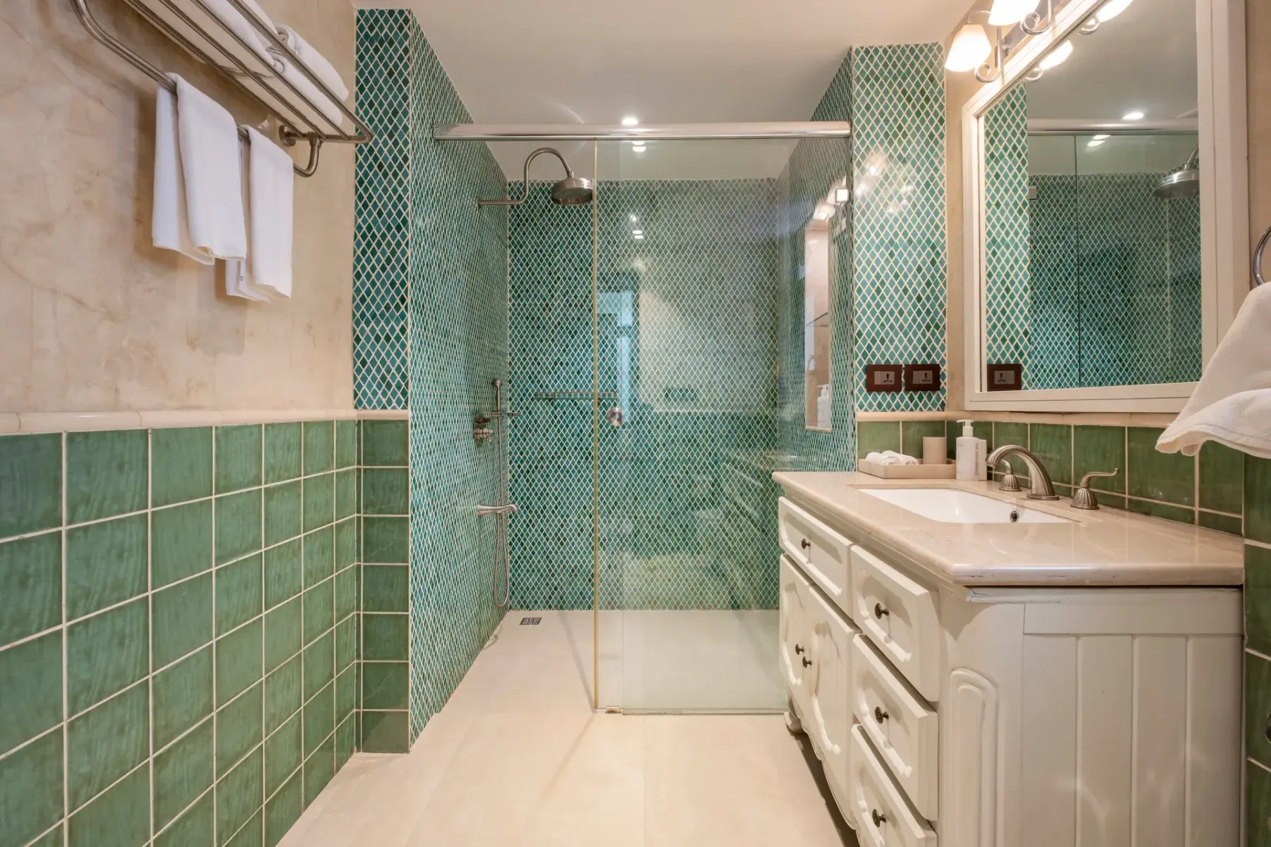 A tiled bathroom with a glass shower, a white vanity, and a large wall mirror.
