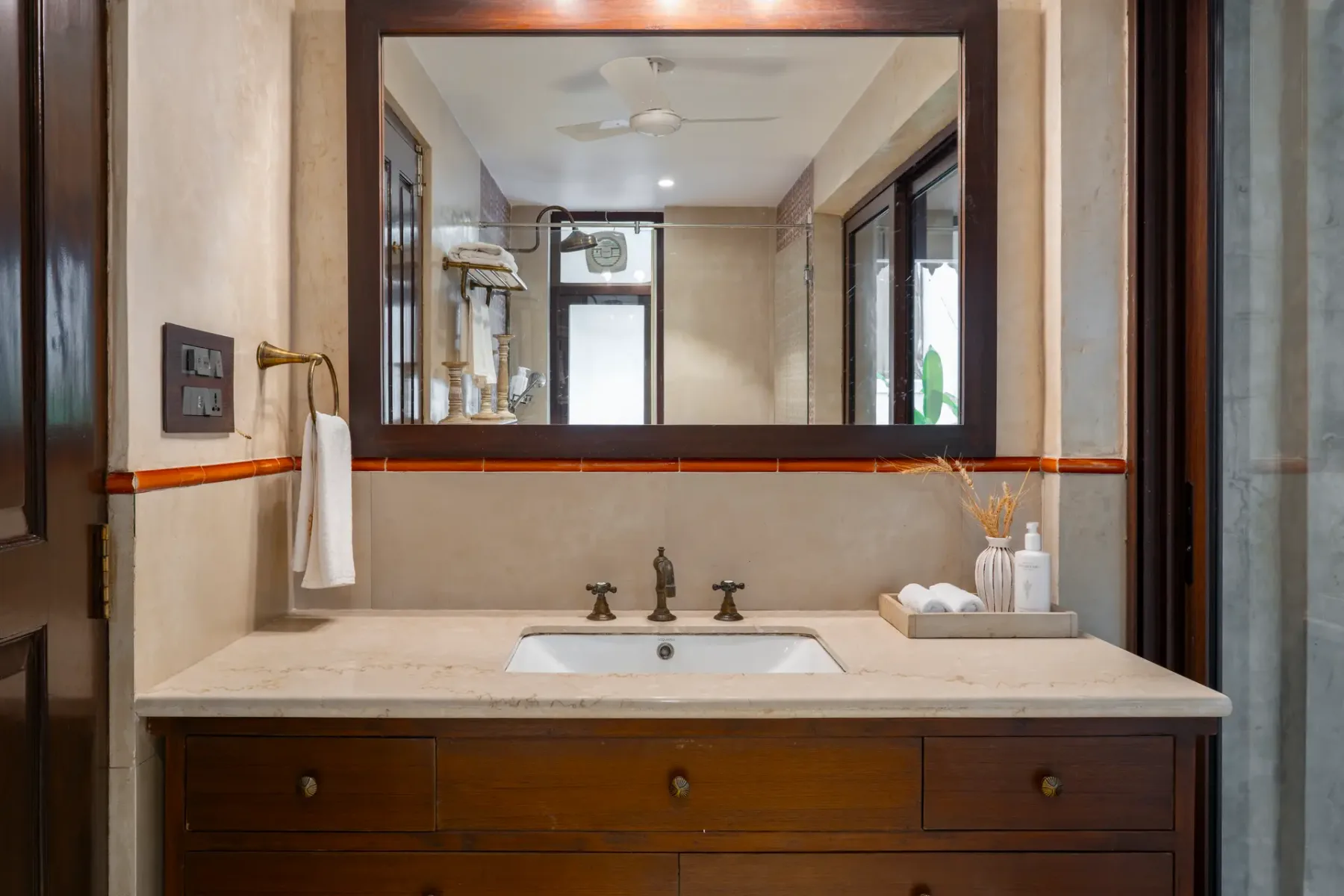 A bathroom vanity with a wide mirror, white sink, dark wood drawers, and toiletries on the counter.