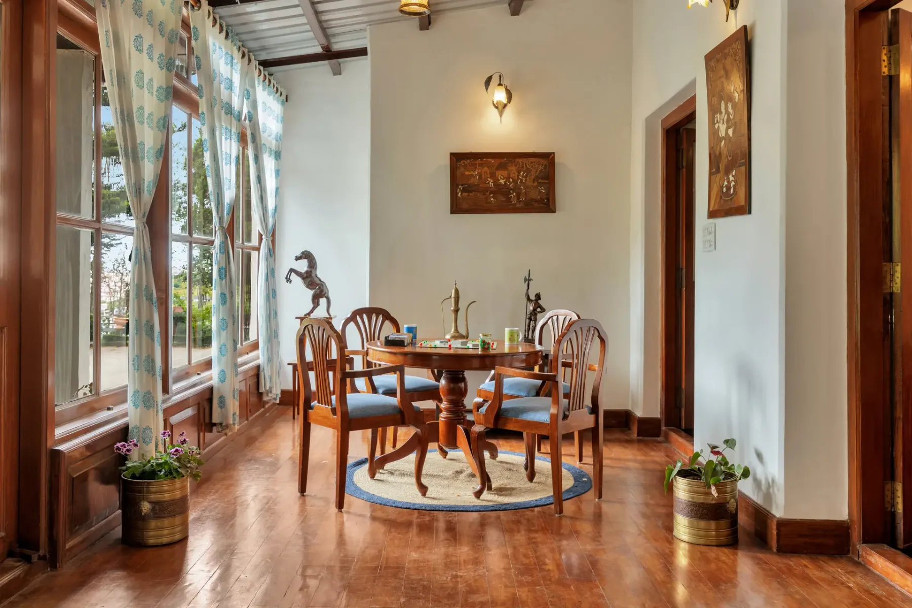 Un comedor con una mesa y sillas de madera junto a grandes ventanas.