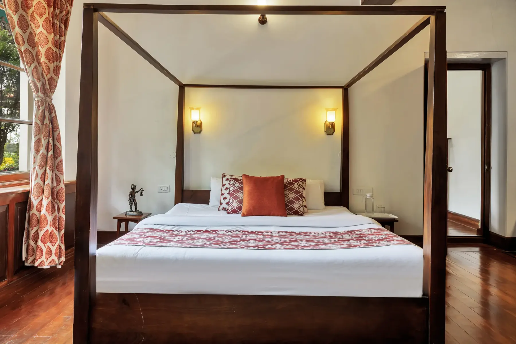 Dormitorio con cama con dosel y cortinas estampadas junto a la ventana.