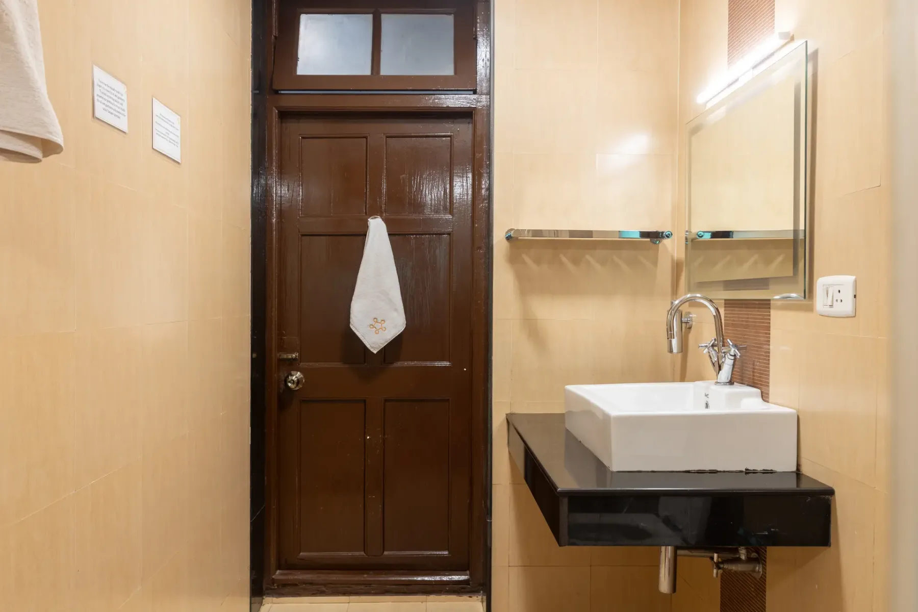 Un baño con un lavabo suspendido y una puerta de madera oscura.