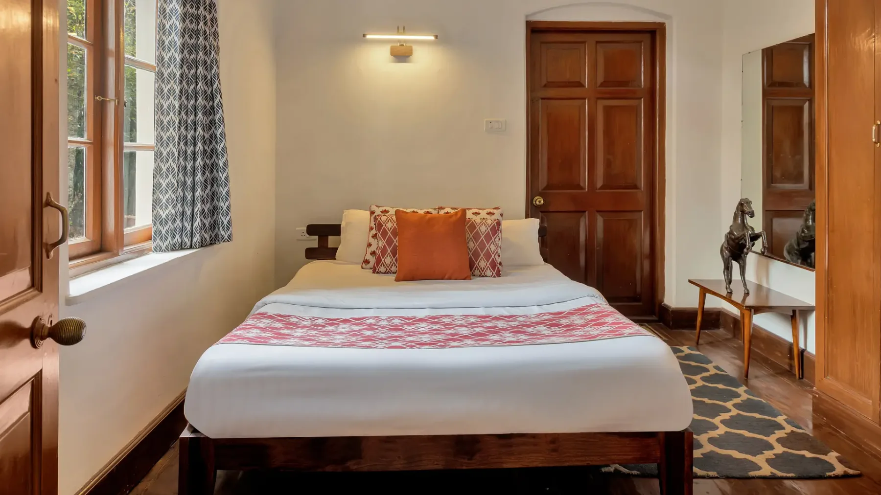 Un dormitorio con una cama tendida, cojines estampados y una ventana.