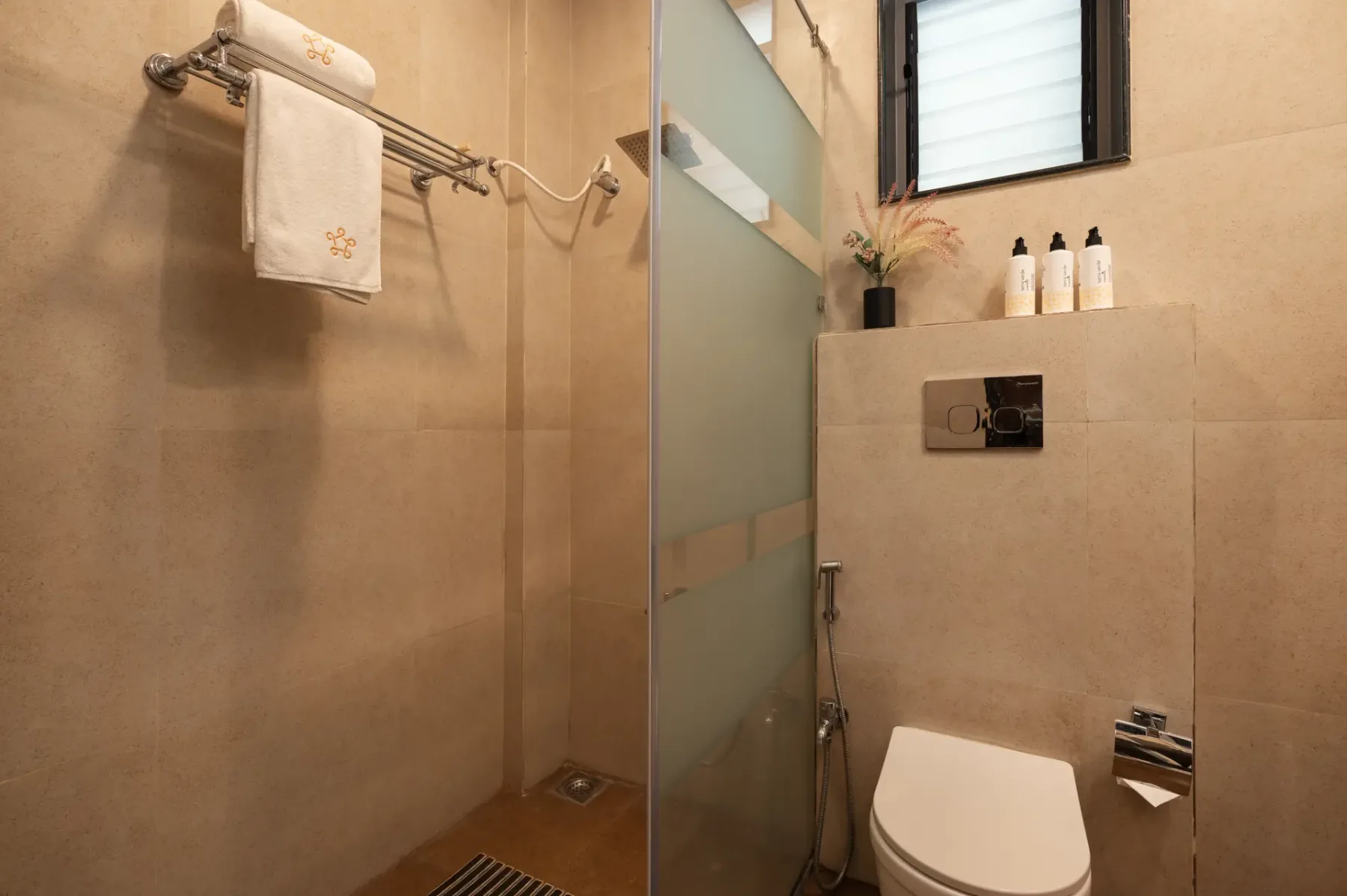 A tiled bathroom with a shower area, toilet, and towel rack.