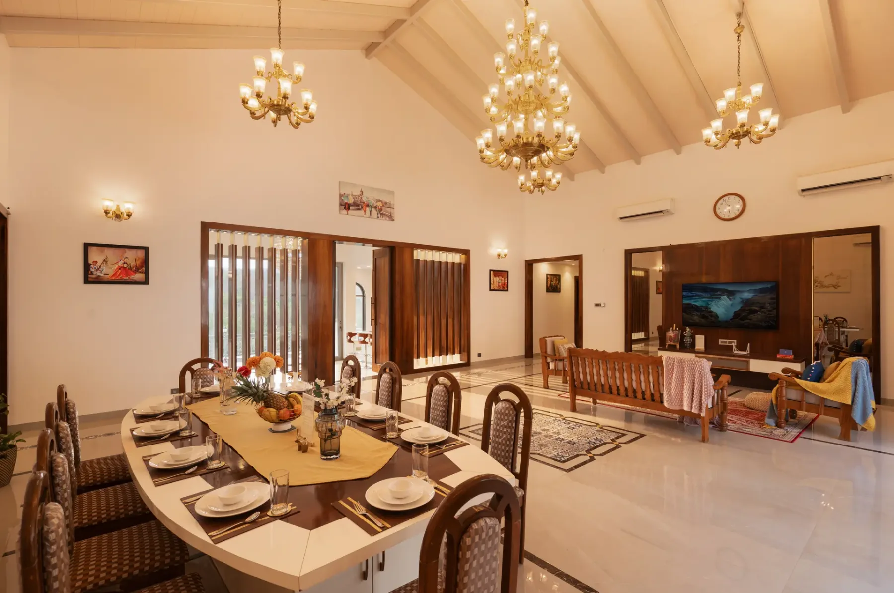 A dining and living room with a long table, chandeliers, and a television.