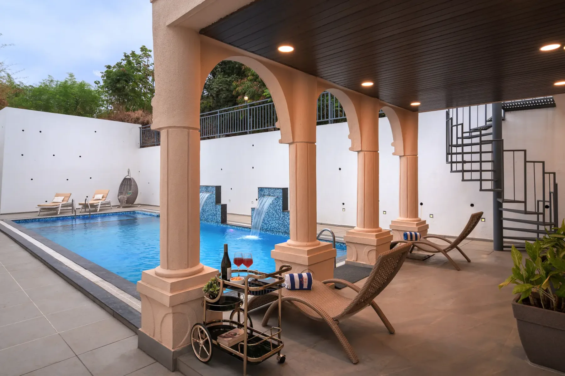 A covered poolside patio with lounge seating overlooks a swimming pool.