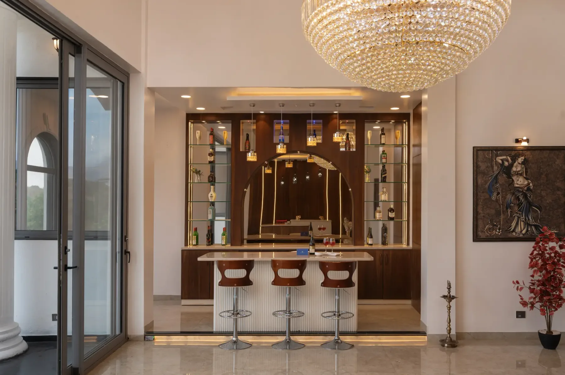 A bar counter with seating stands beneath a large chandelier.