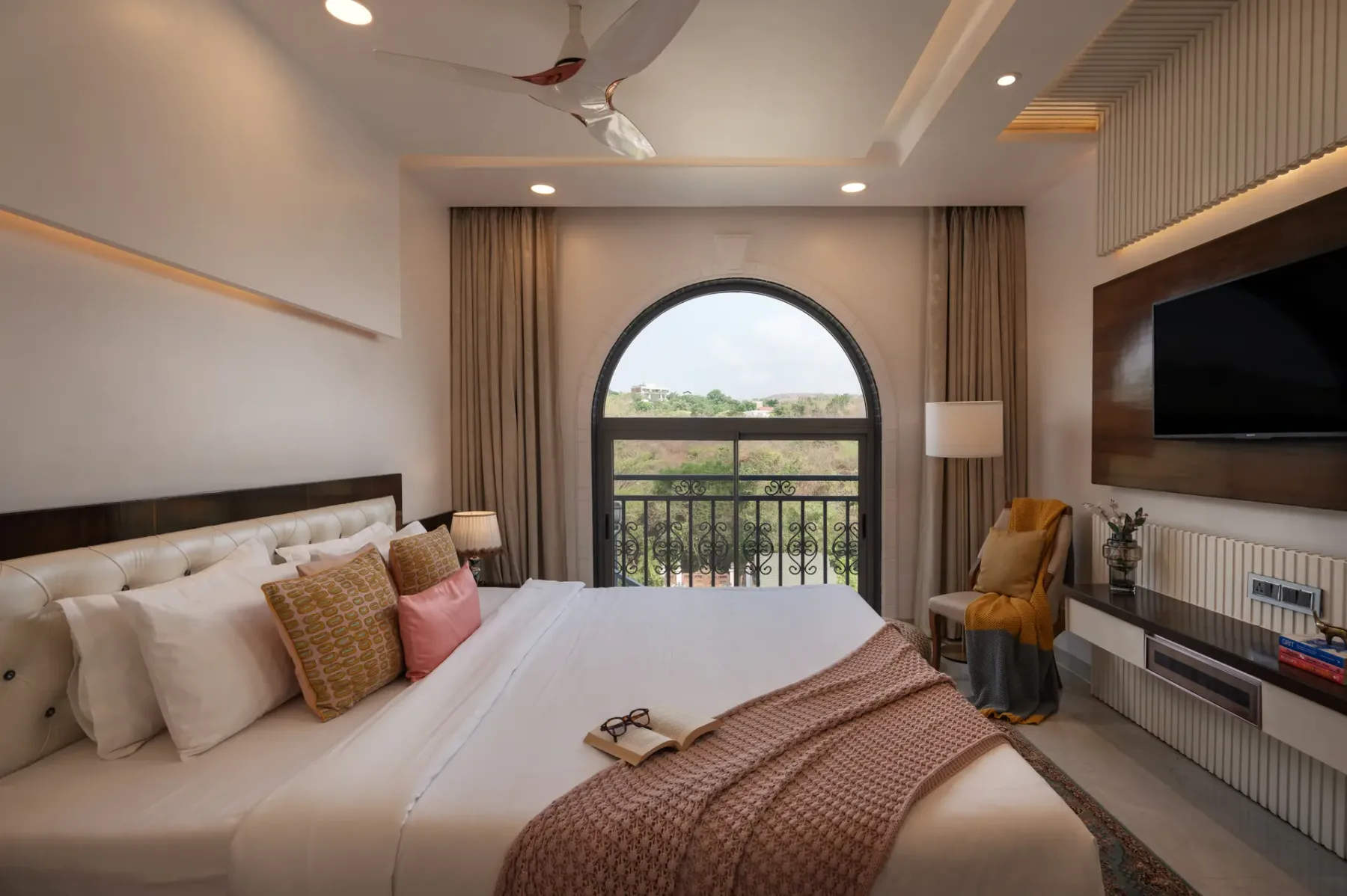 A bedroom with a large bed, an arched window, and a wall-mounted television.