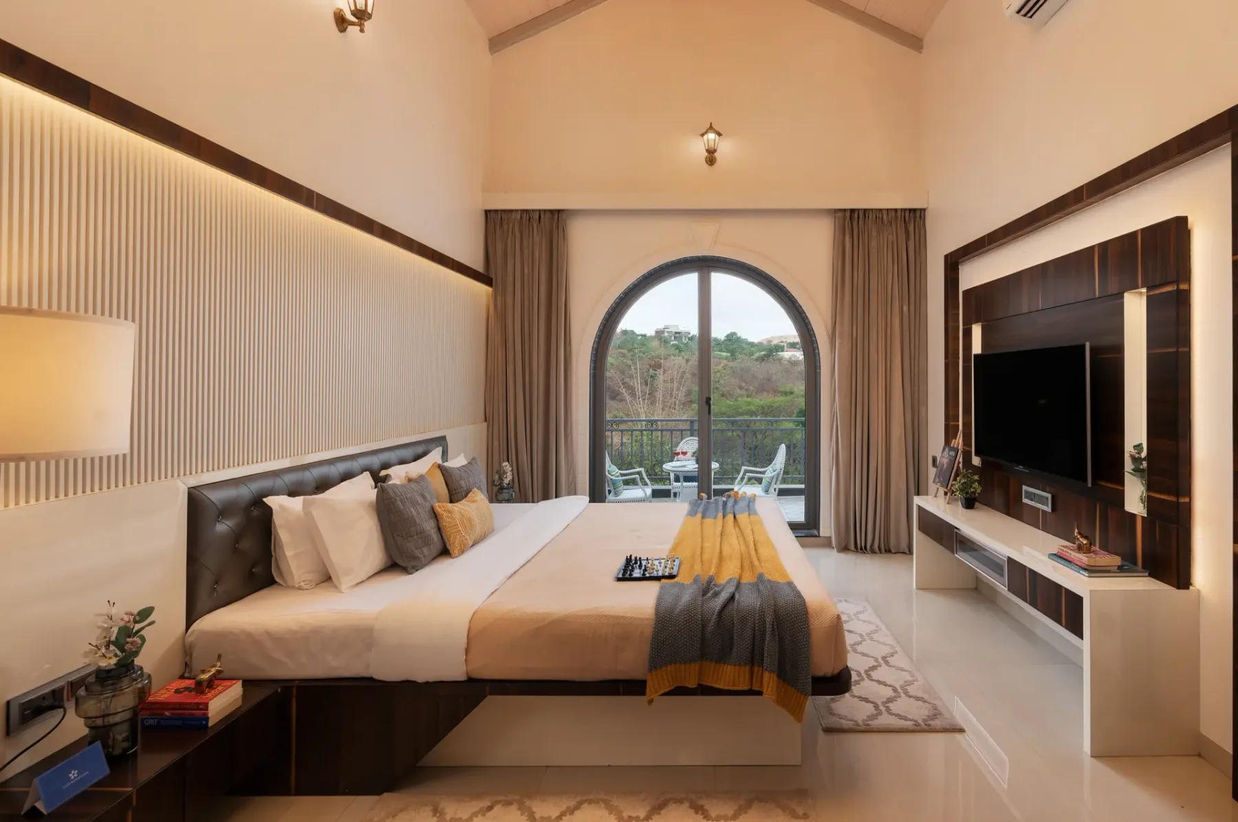 A bedroom with a bed facing a wall-mounted television and an arched window.
