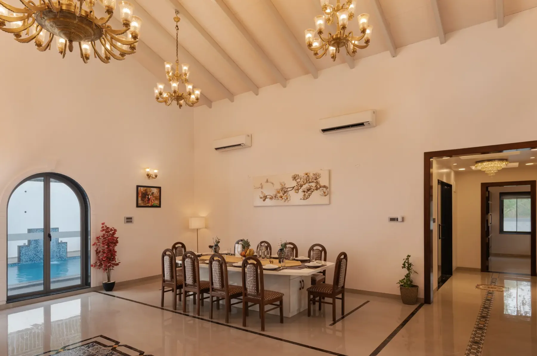 A dining area with a long table and chairs beneath hanging chandeliers.