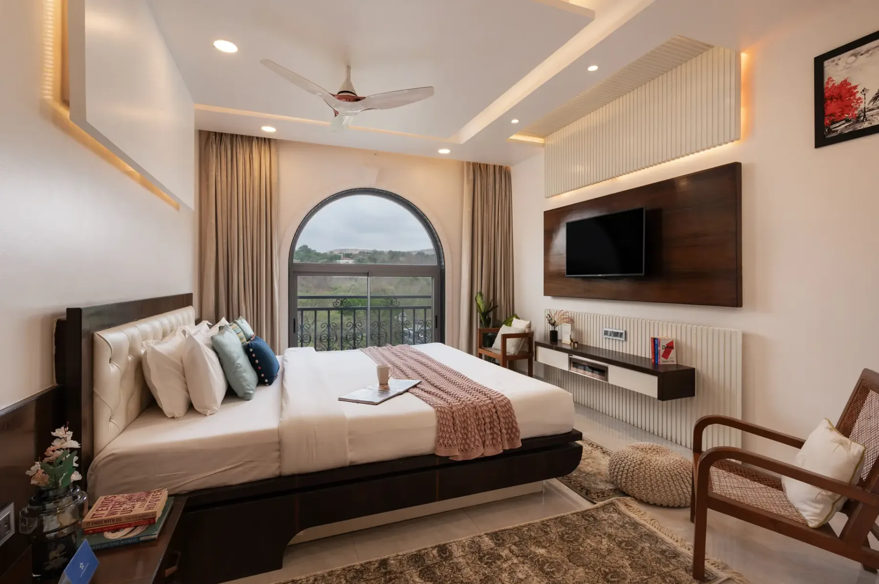 A bedroom with a bed, an arched window, and a wall-mounted television.