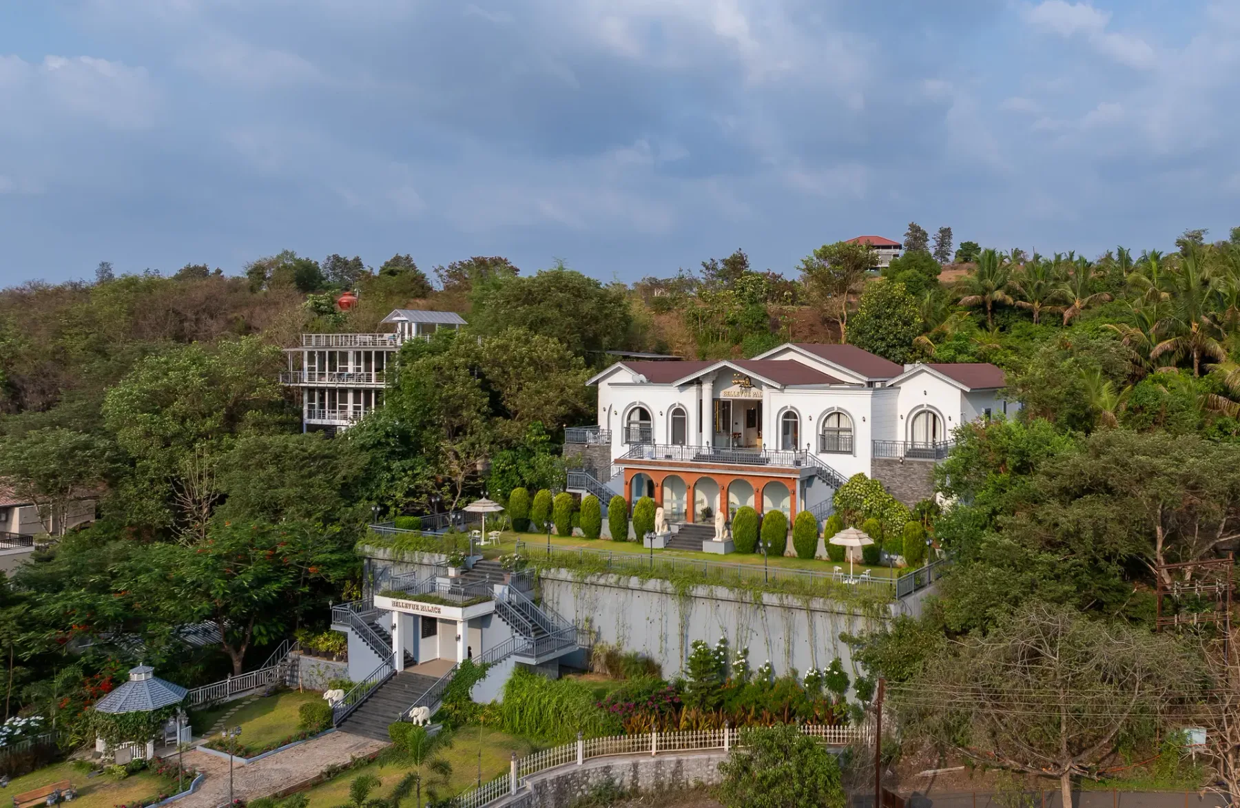 A large white villa sits among green trees on a hillside.