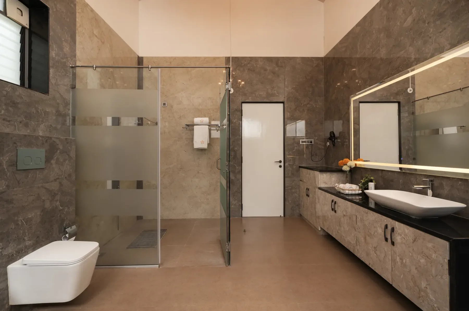 A modern bathroom with a glass shower, wall-mounted toilet, and long vanity.