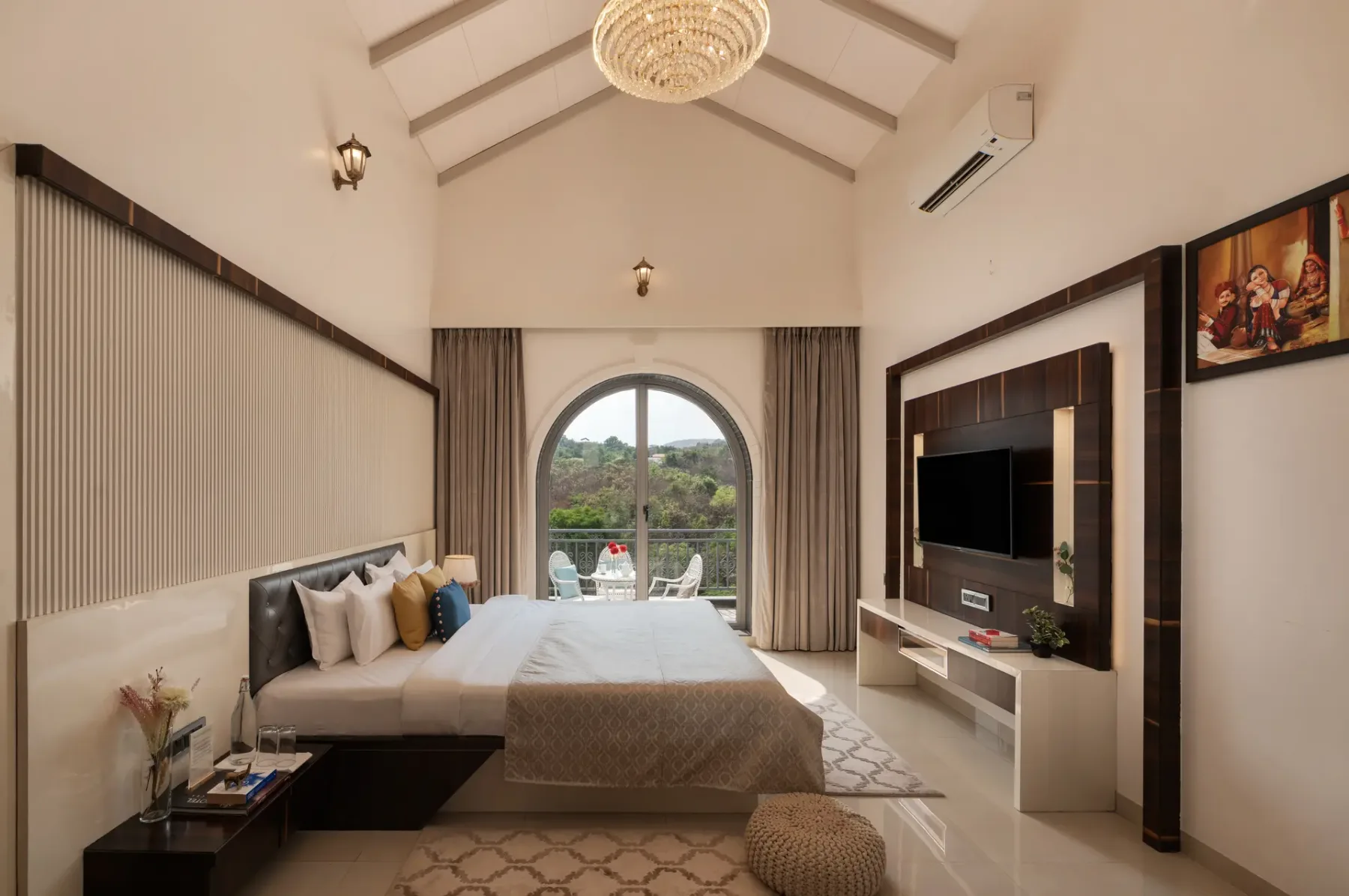 A bedroom with a bed, television, and arched window overlooking greenery.