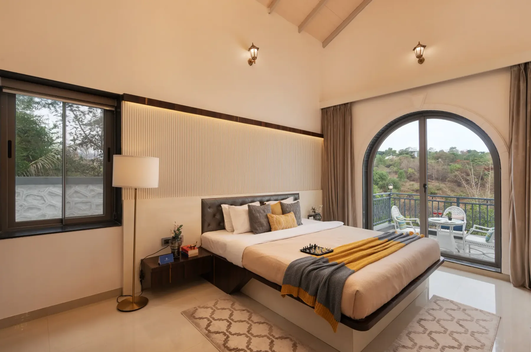 A bedroom with a bed beside an arched glass door opening onto a balcony.