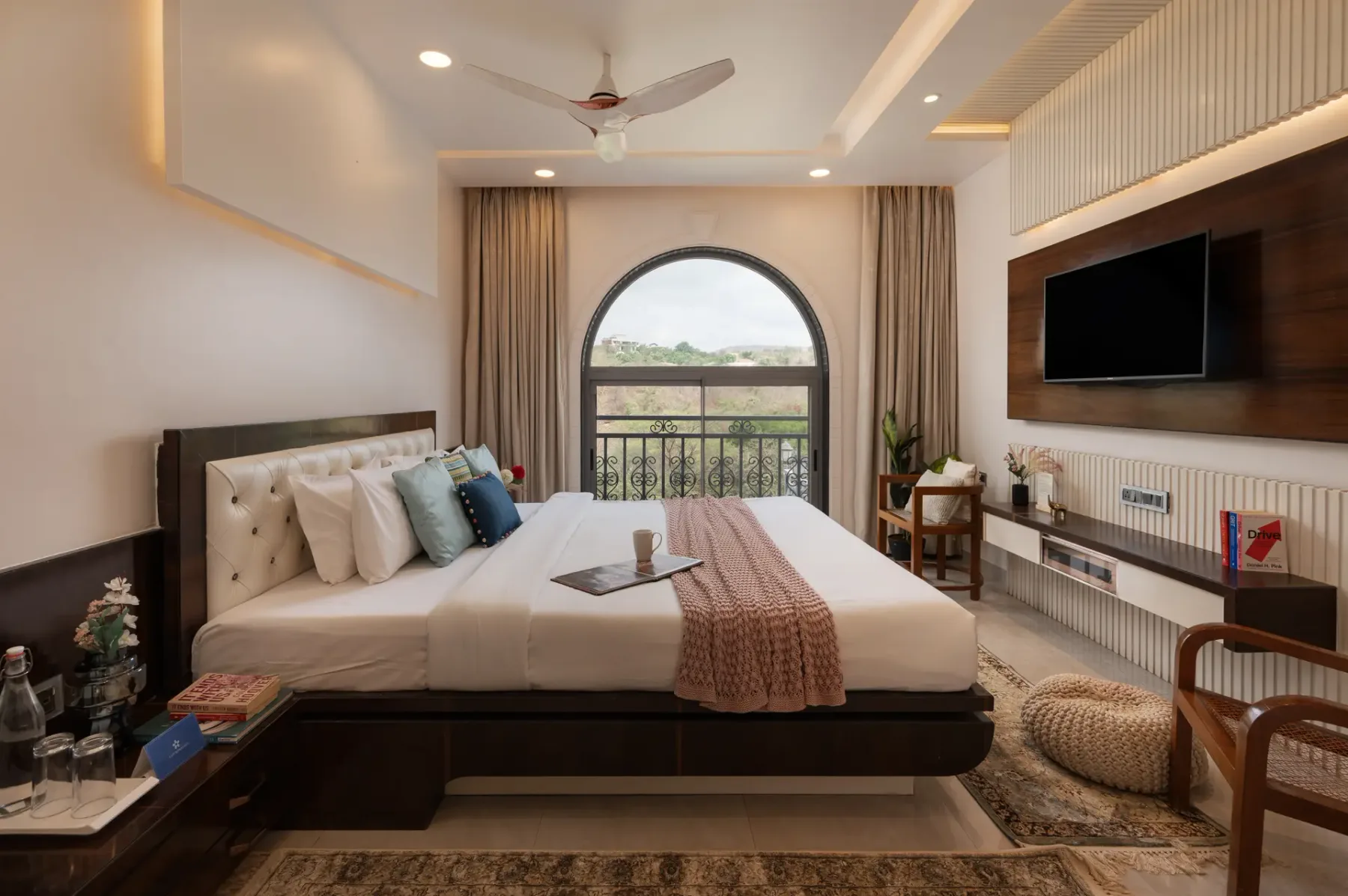 A bedroom with a large bed, an arched window, and a wall-mounted television.