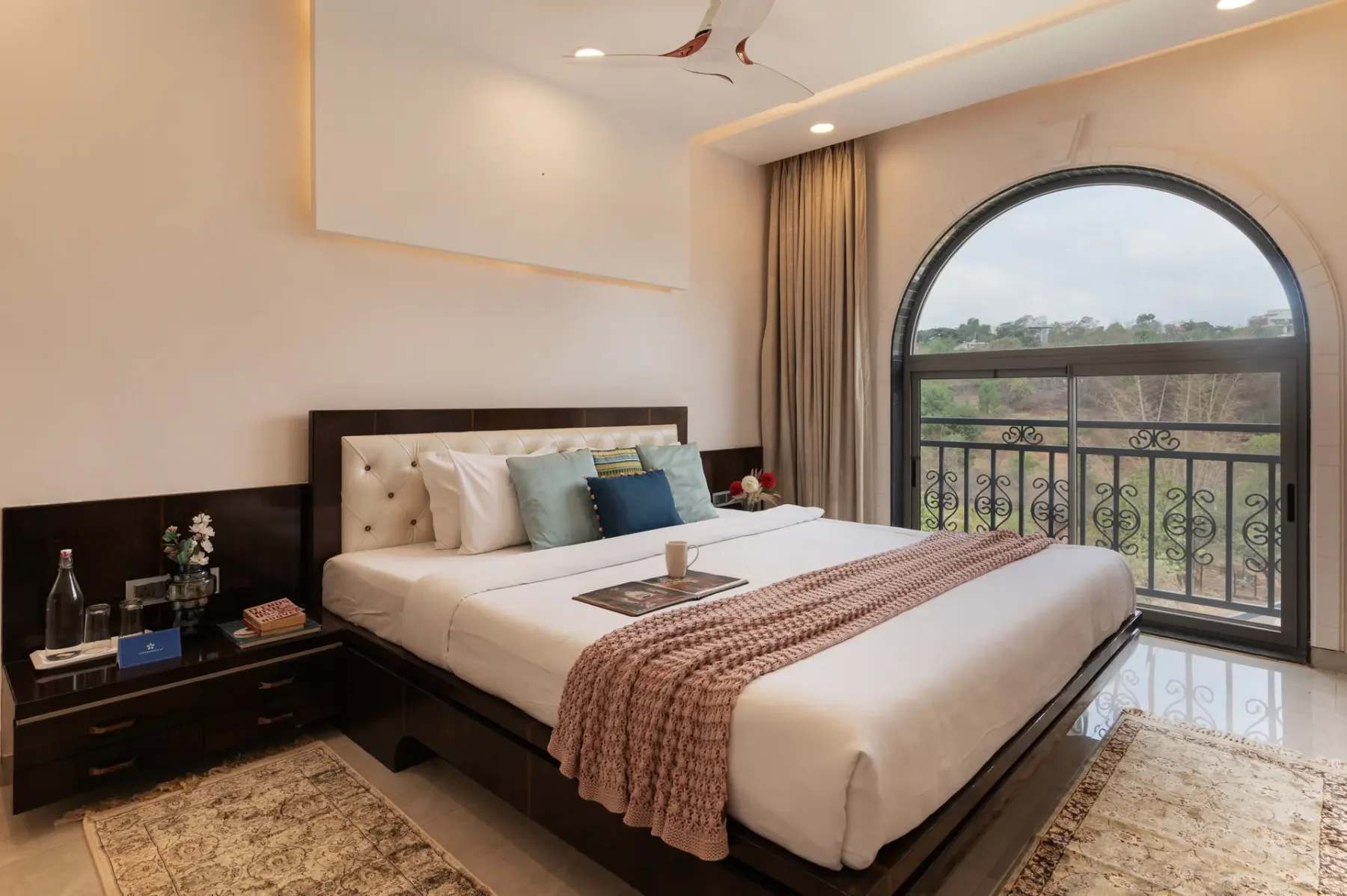 A bedroom with a neatly made bed beside a large arched window.