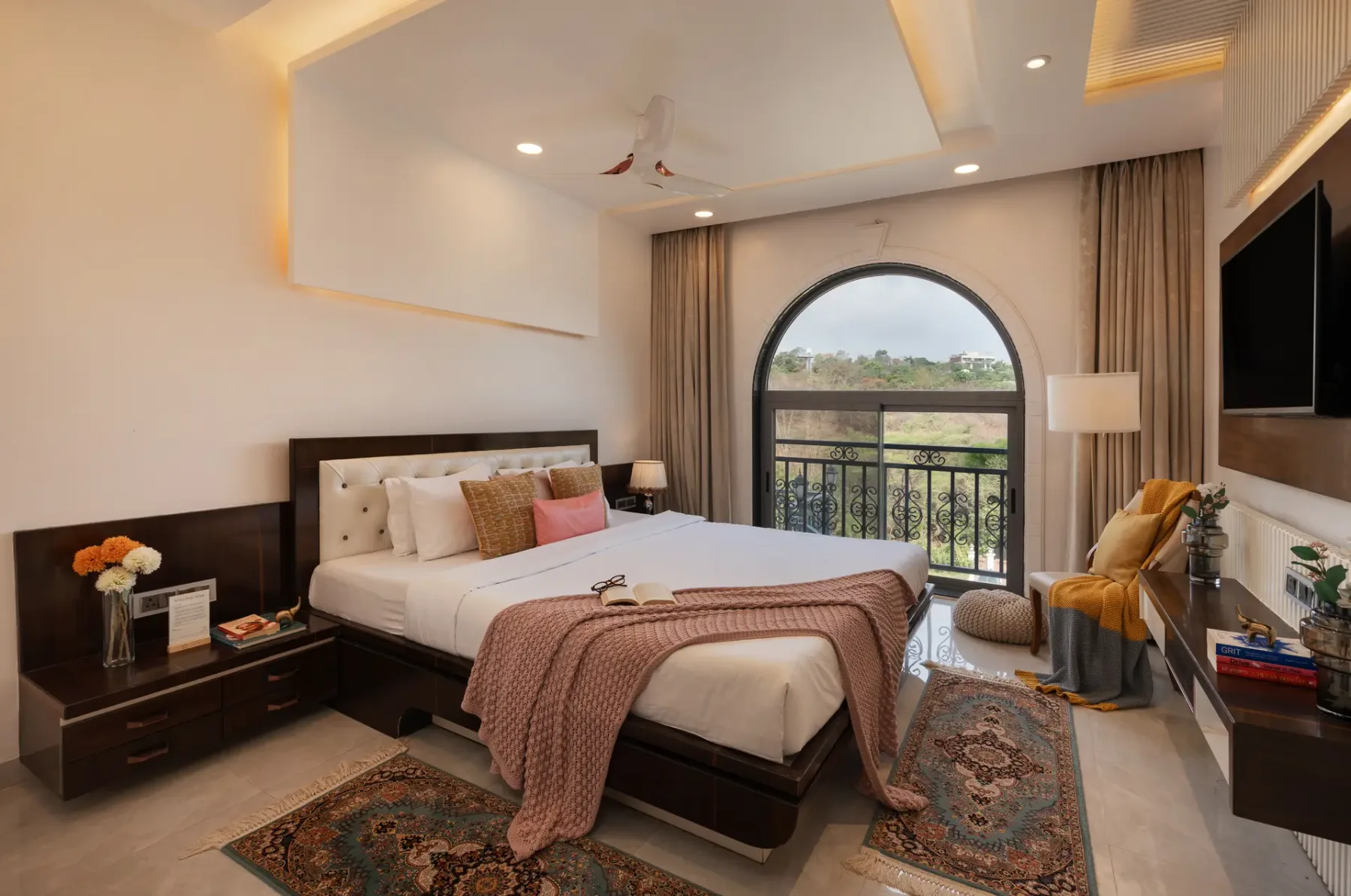 A bedroom with a bed facing an arched window and balcony railing.