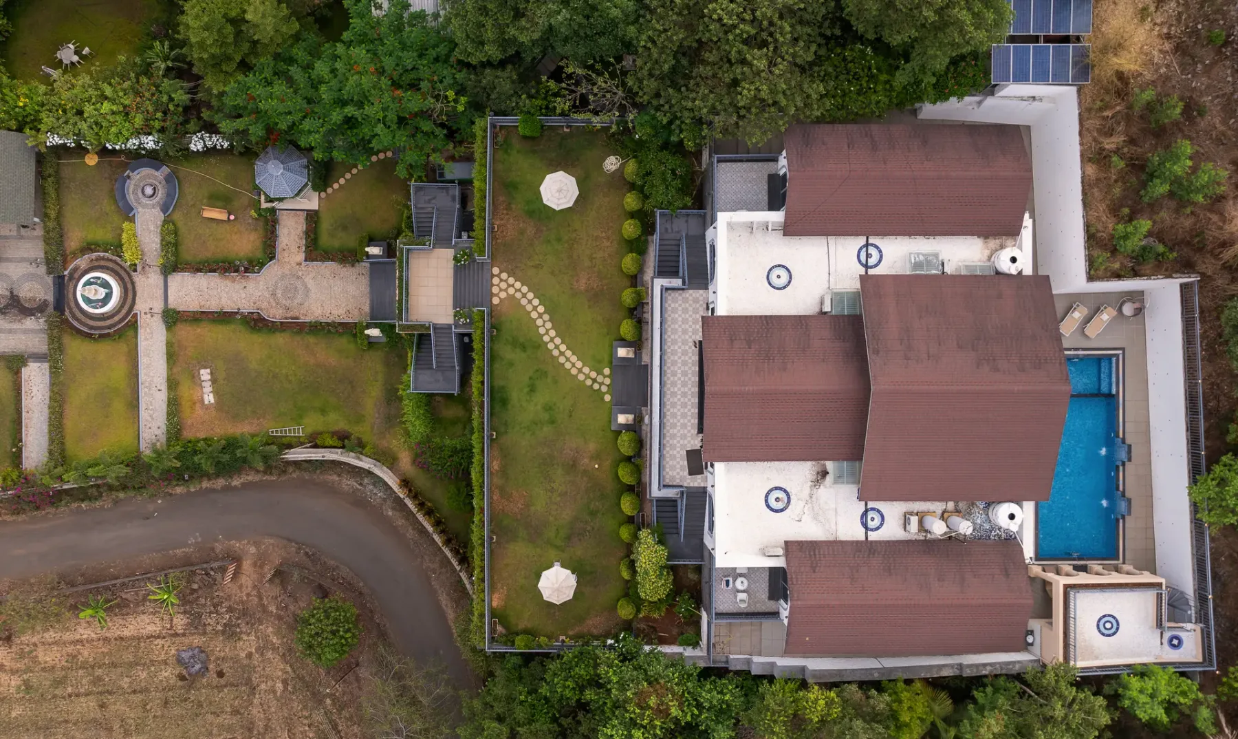 An aerial view of a building with several roof sections beside a blue swimming pool.
