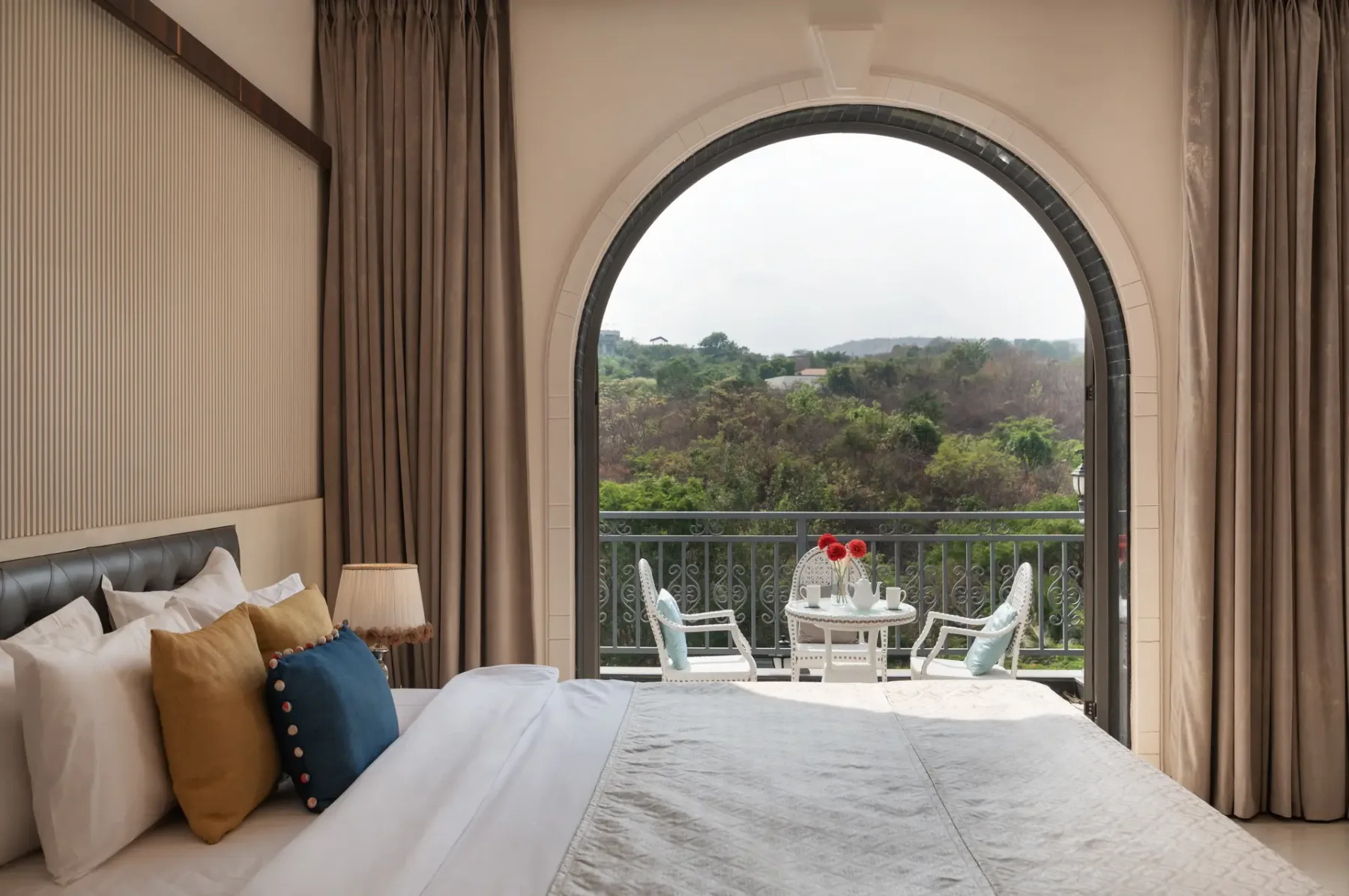 A bedroom with a bed facing an arched window and a small balcony seating area.