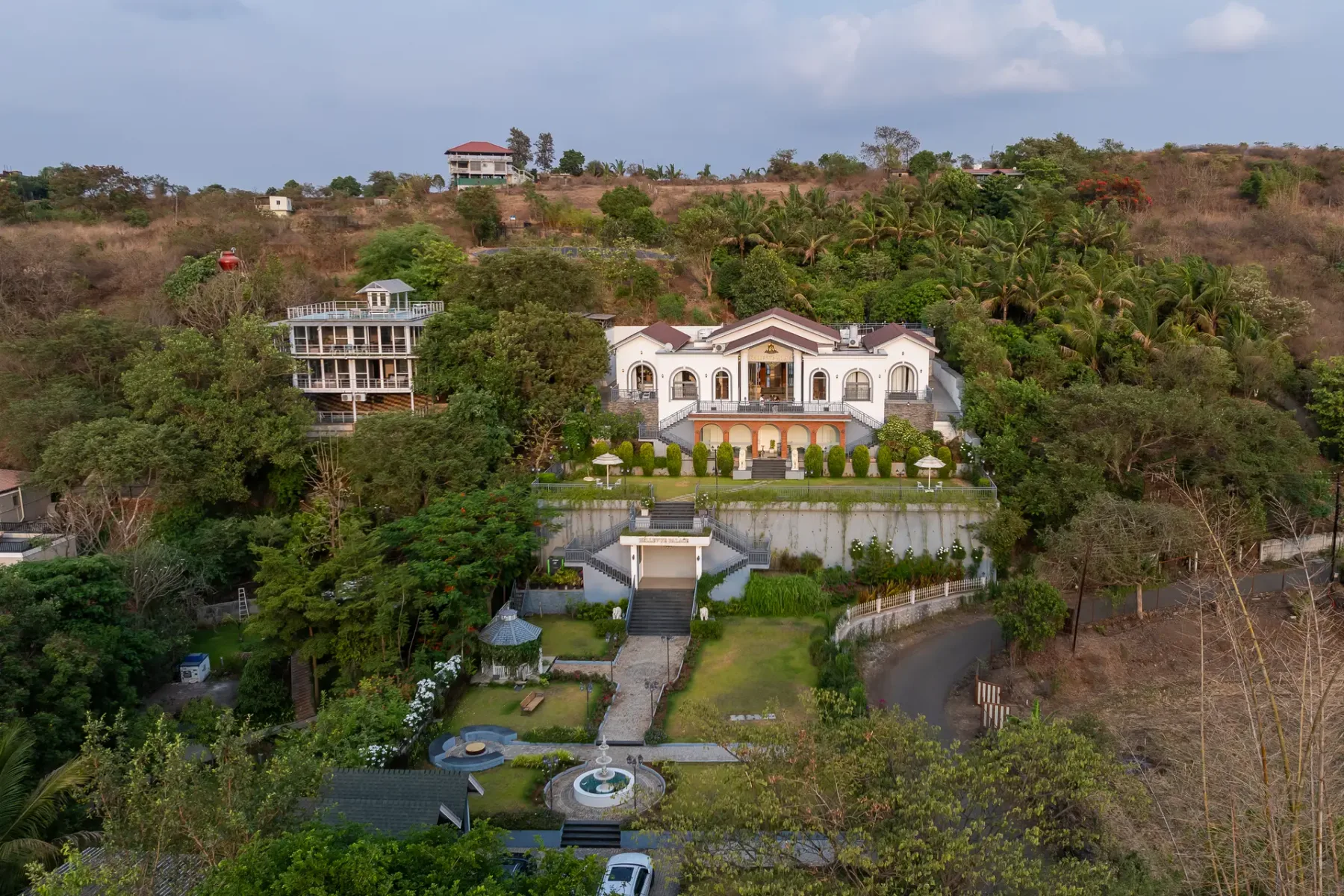 A large villa stands amid landscaped grounds on a wooded hillside.