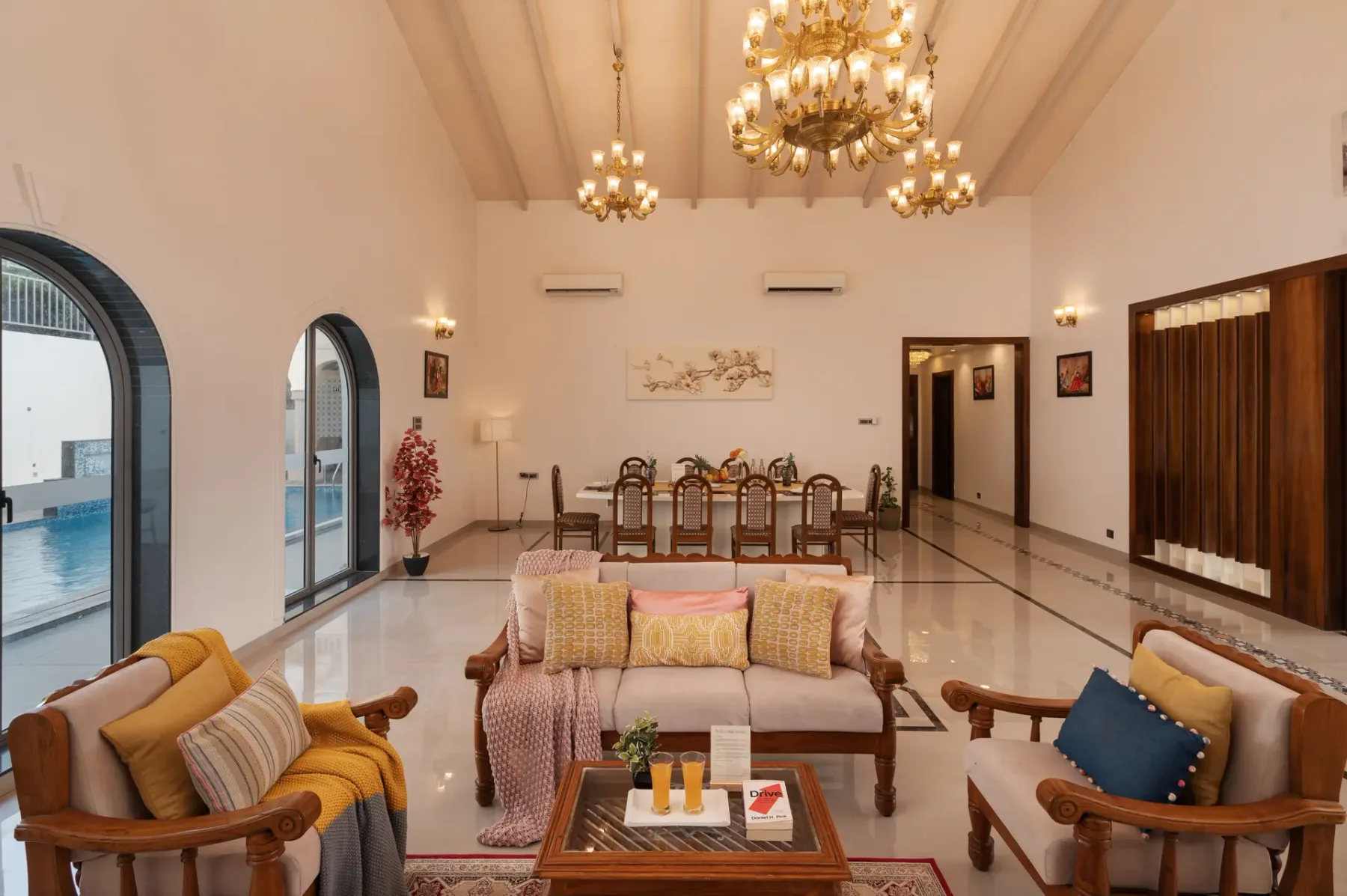 A spacious living and dining room with seating, a dining table, and chandeliers.