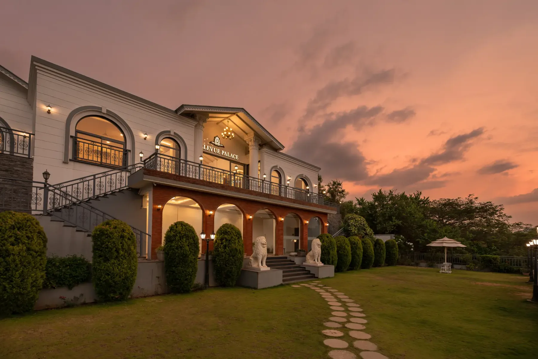 A large building stands beside a manicured lawn under a colorful sunset sky.