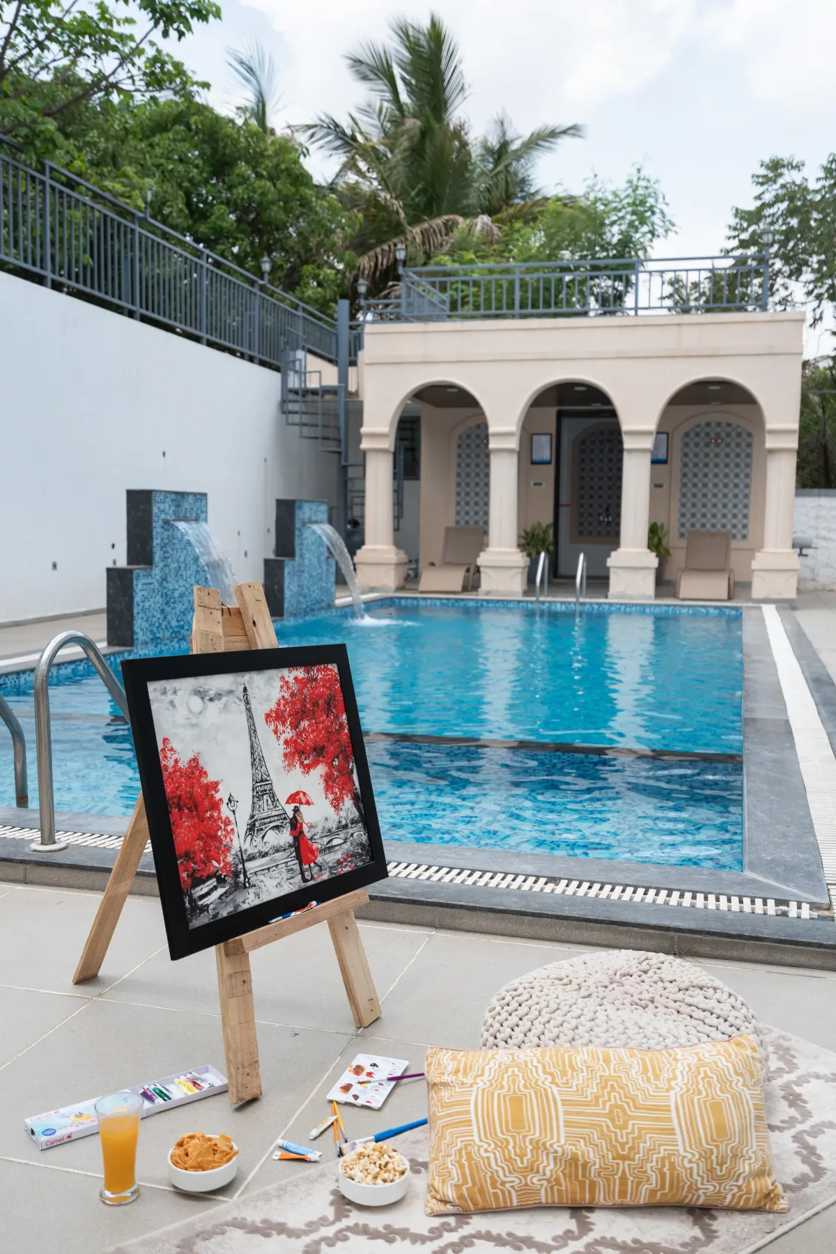 An outdoor swimming pool beside a small arched pavilion, with an easel in the foreground.