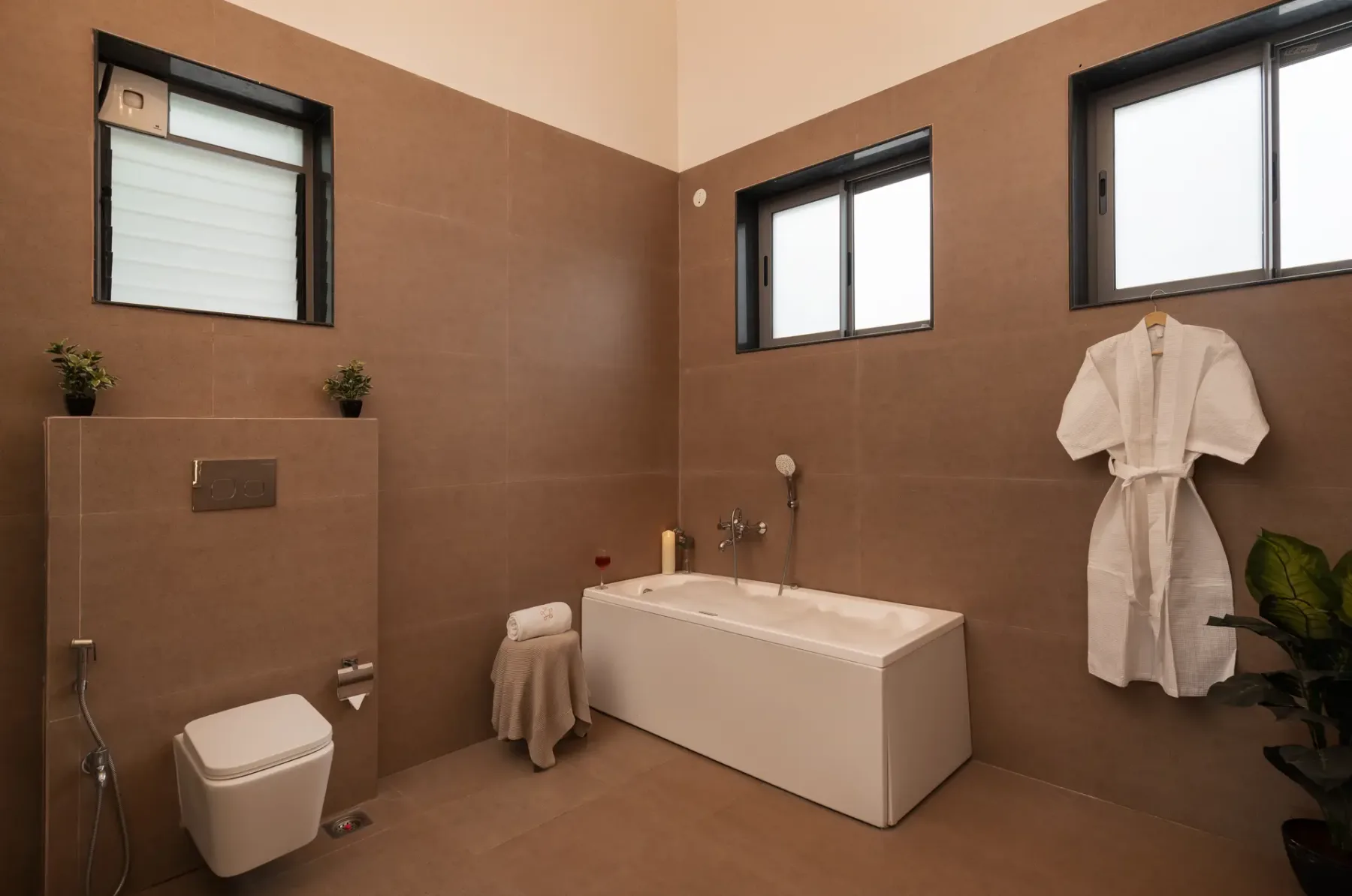 A tiled bathroom with a bathtub, wall-mounted toilet, and windows.