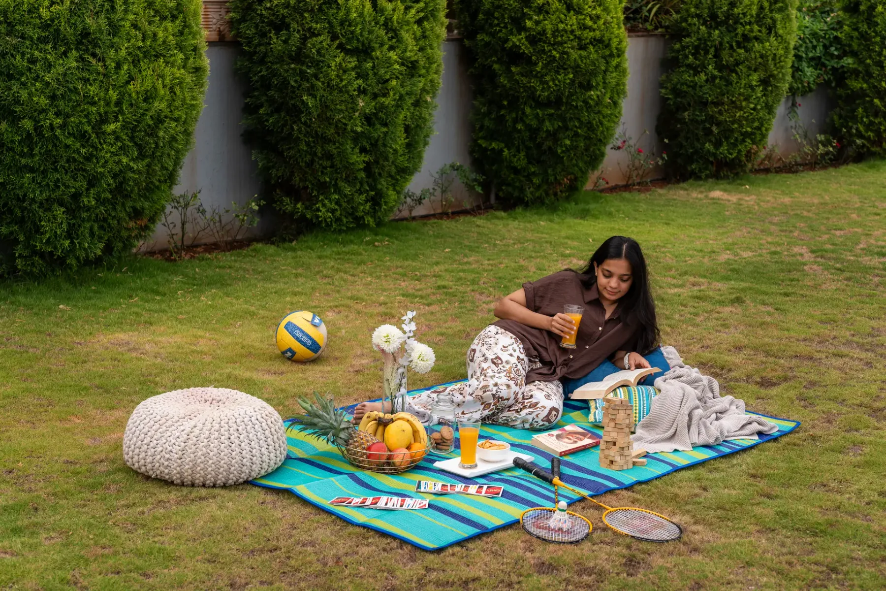 A woman relaxes on a picnic blanket in a grassy yard.