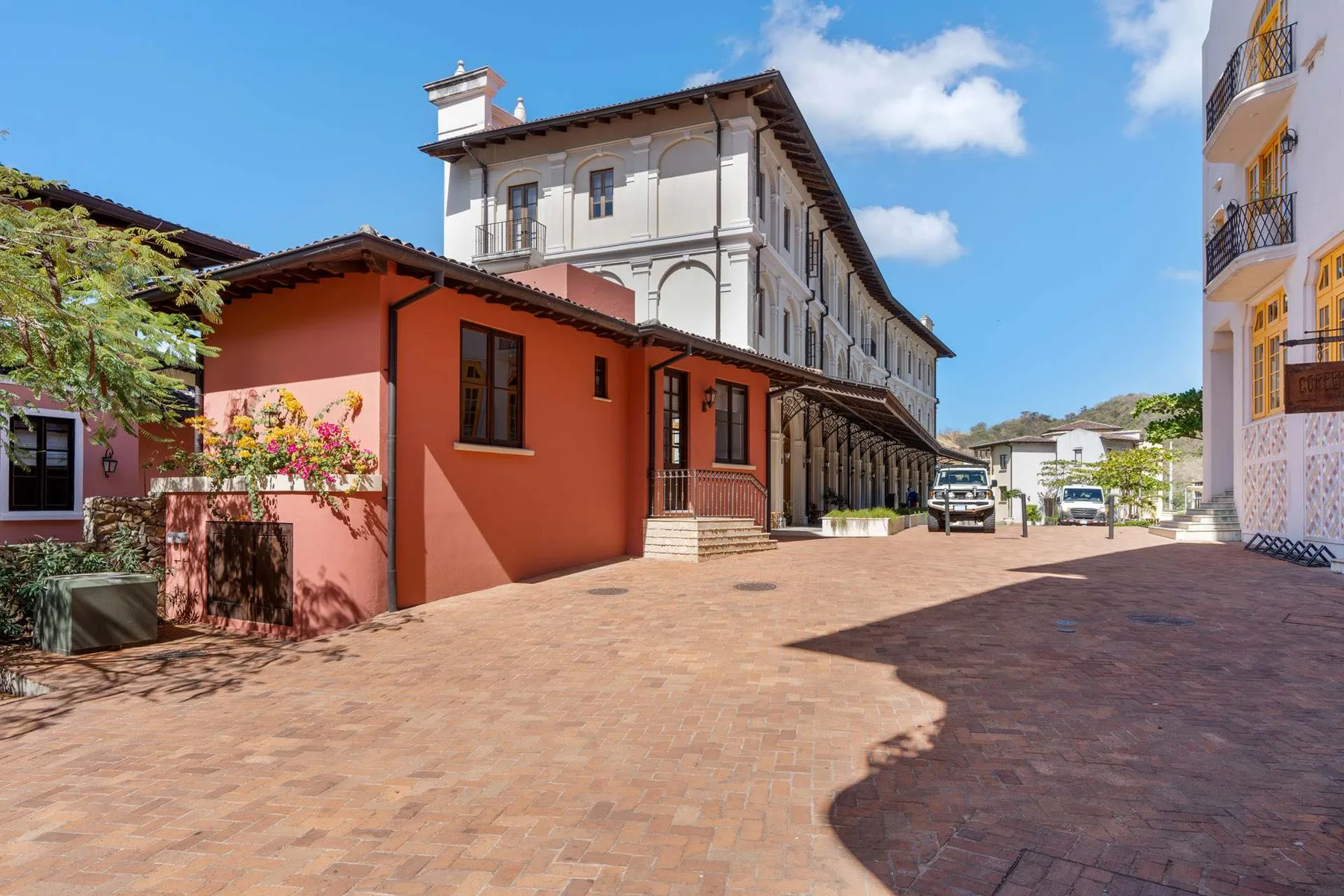 A paved courtyard sits between colorful buildings under a clear blue sky.