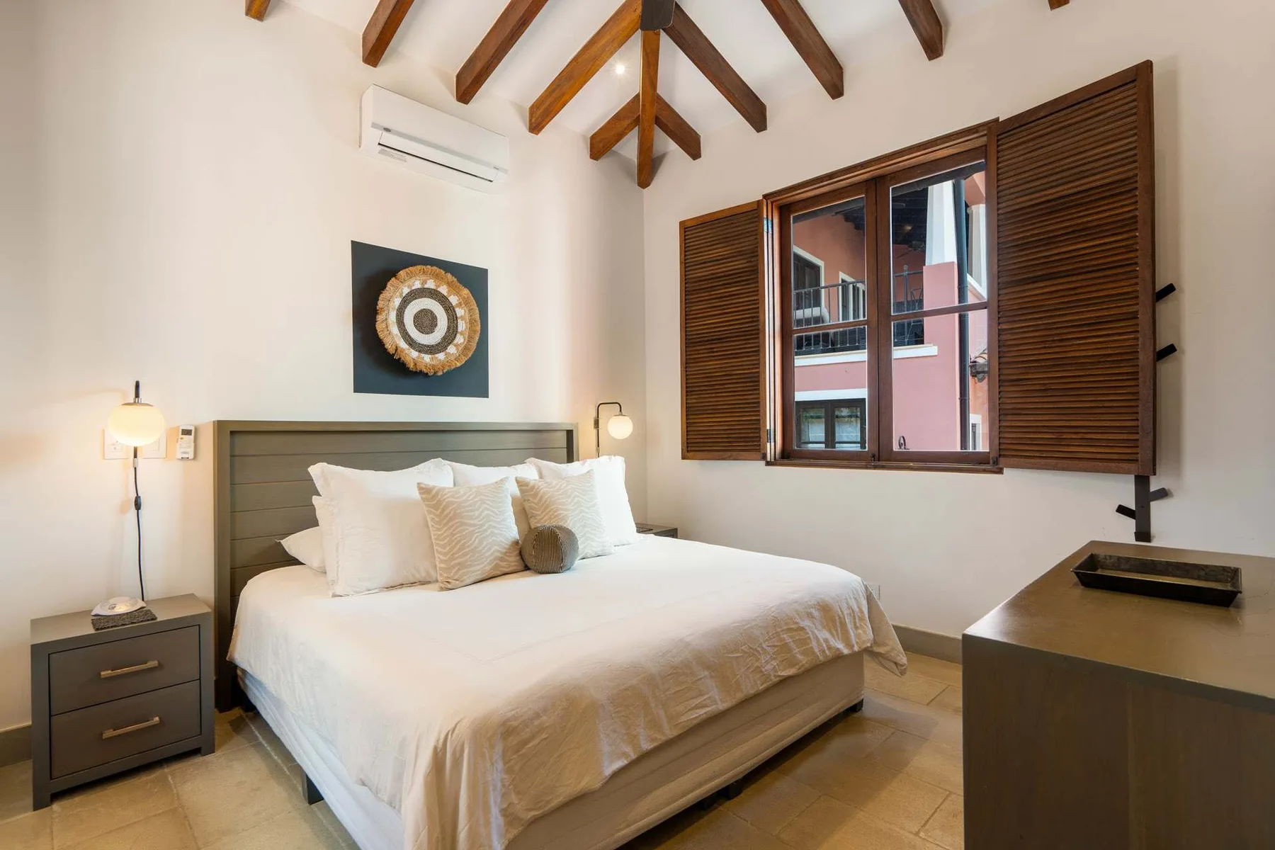 A bedroom with a large bed beneath exposed wooden ceiling beams.
