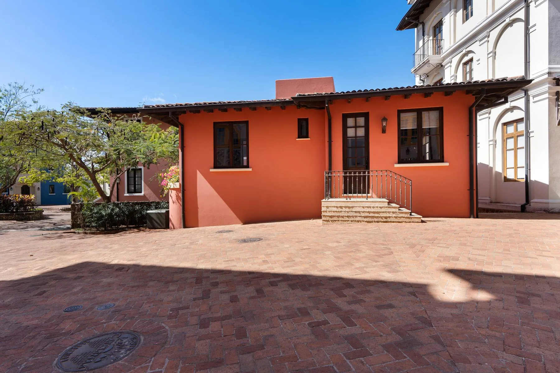 An orange building with windows and steps opens onto a paved courtyard.