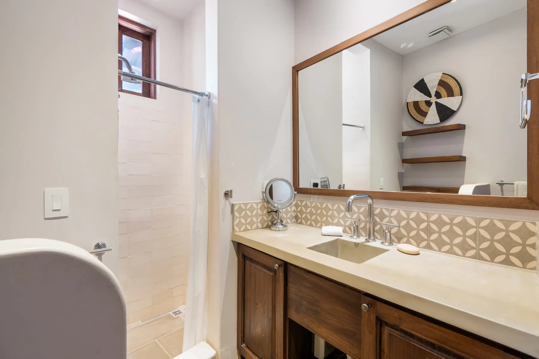 A bathroom vanity with a large mirror sits beside a tiled shower.