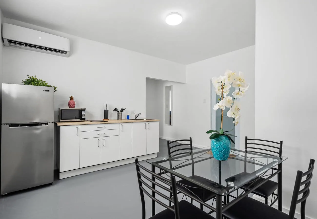 A bright kitchen and dining area with white cabinets and a glass-top table.