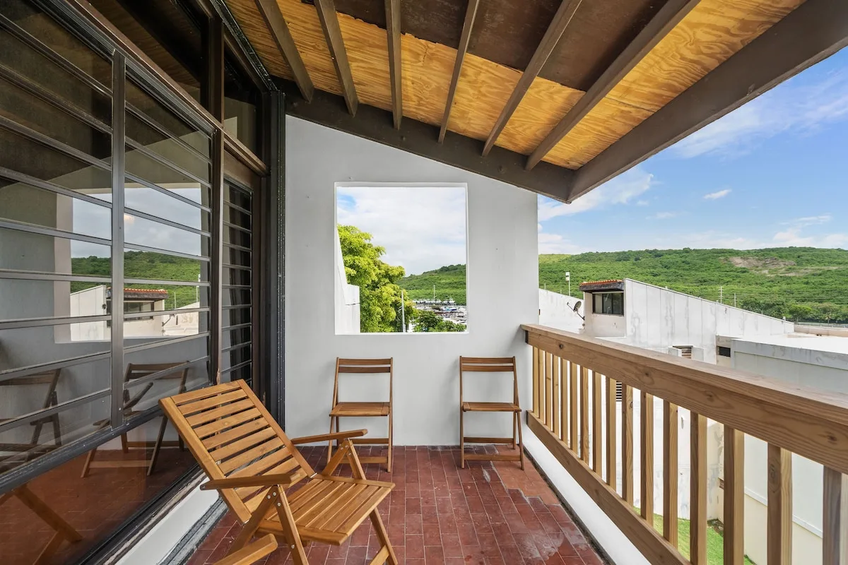 A covered balcony with wooden seating overlooks green hills.