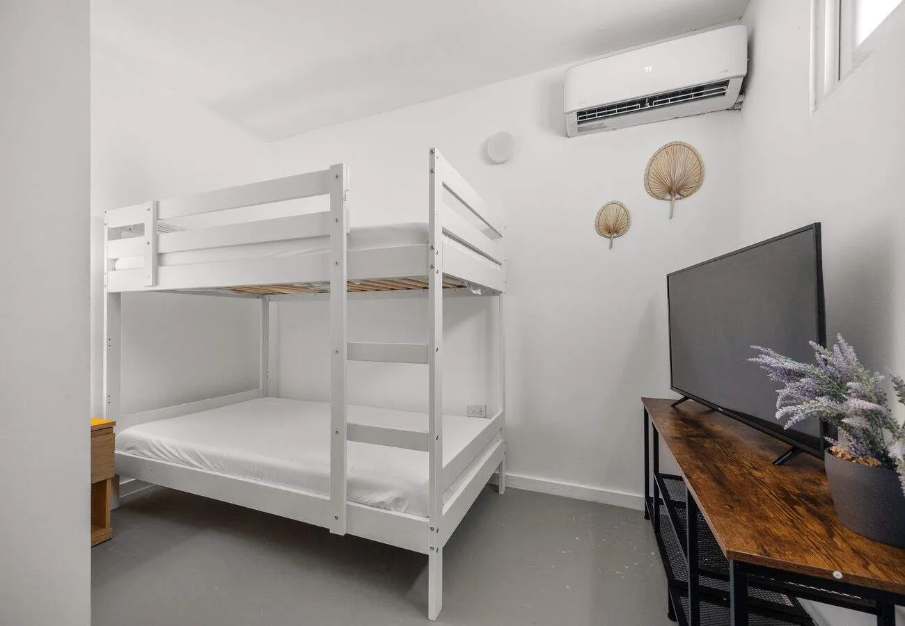 A bright bedroom with a white bunk bed and a television on a wooden table.