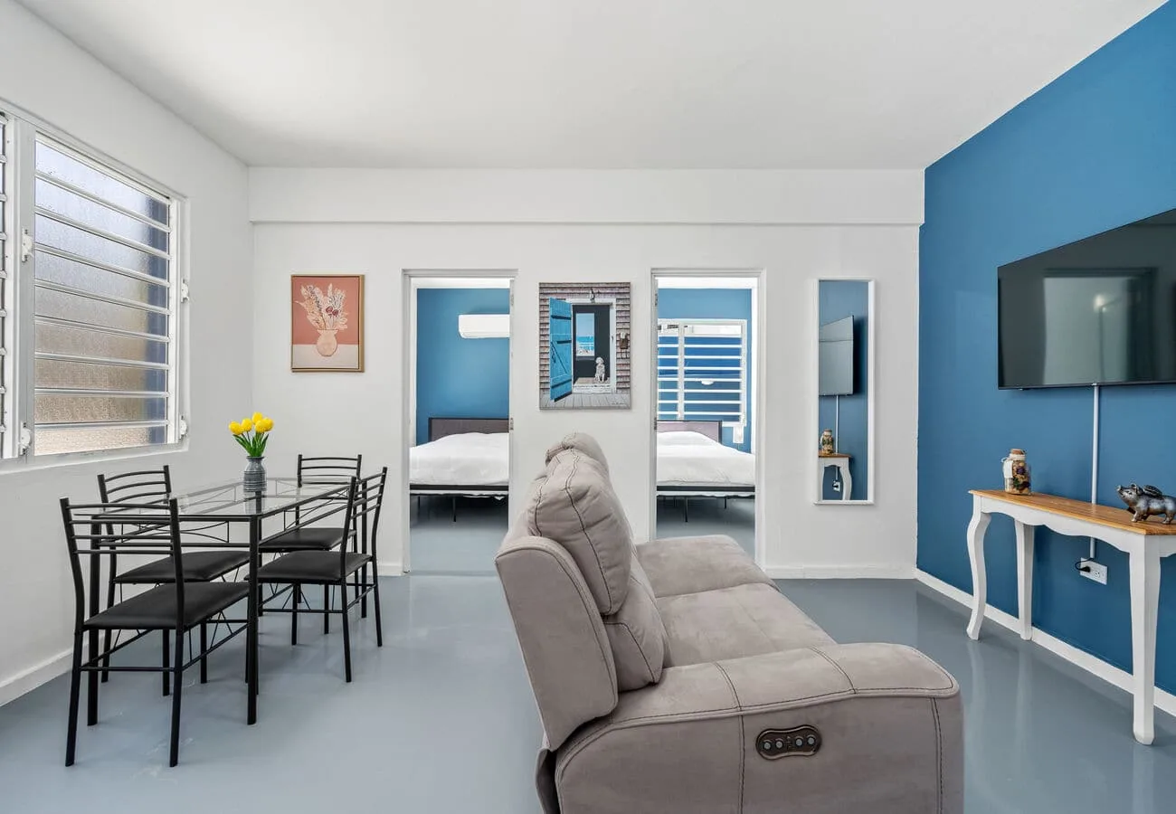A living area with seating, a dining table, and open doorways to adjoining rooms.