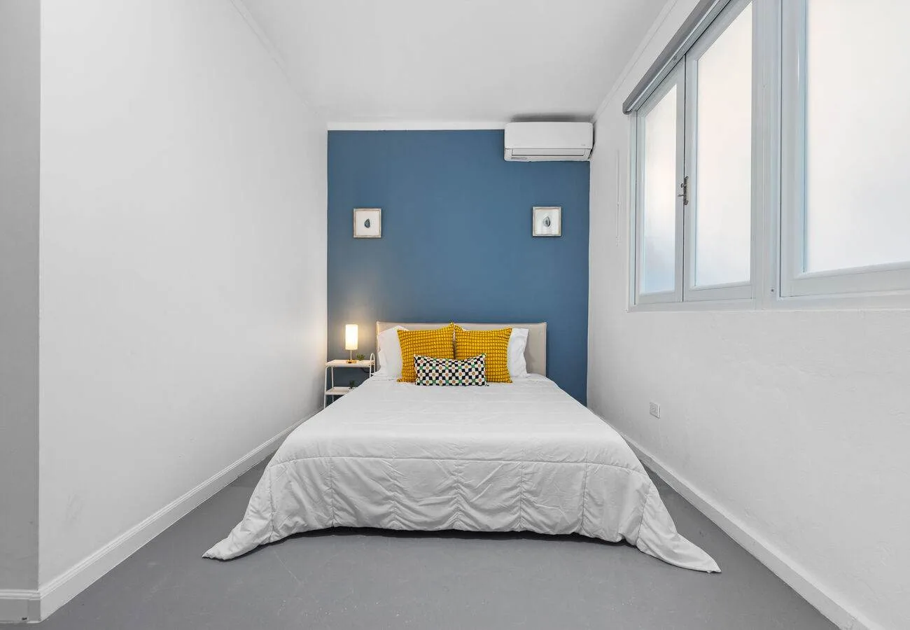 A bedroom with a bed against a blue wall and windows along one side.