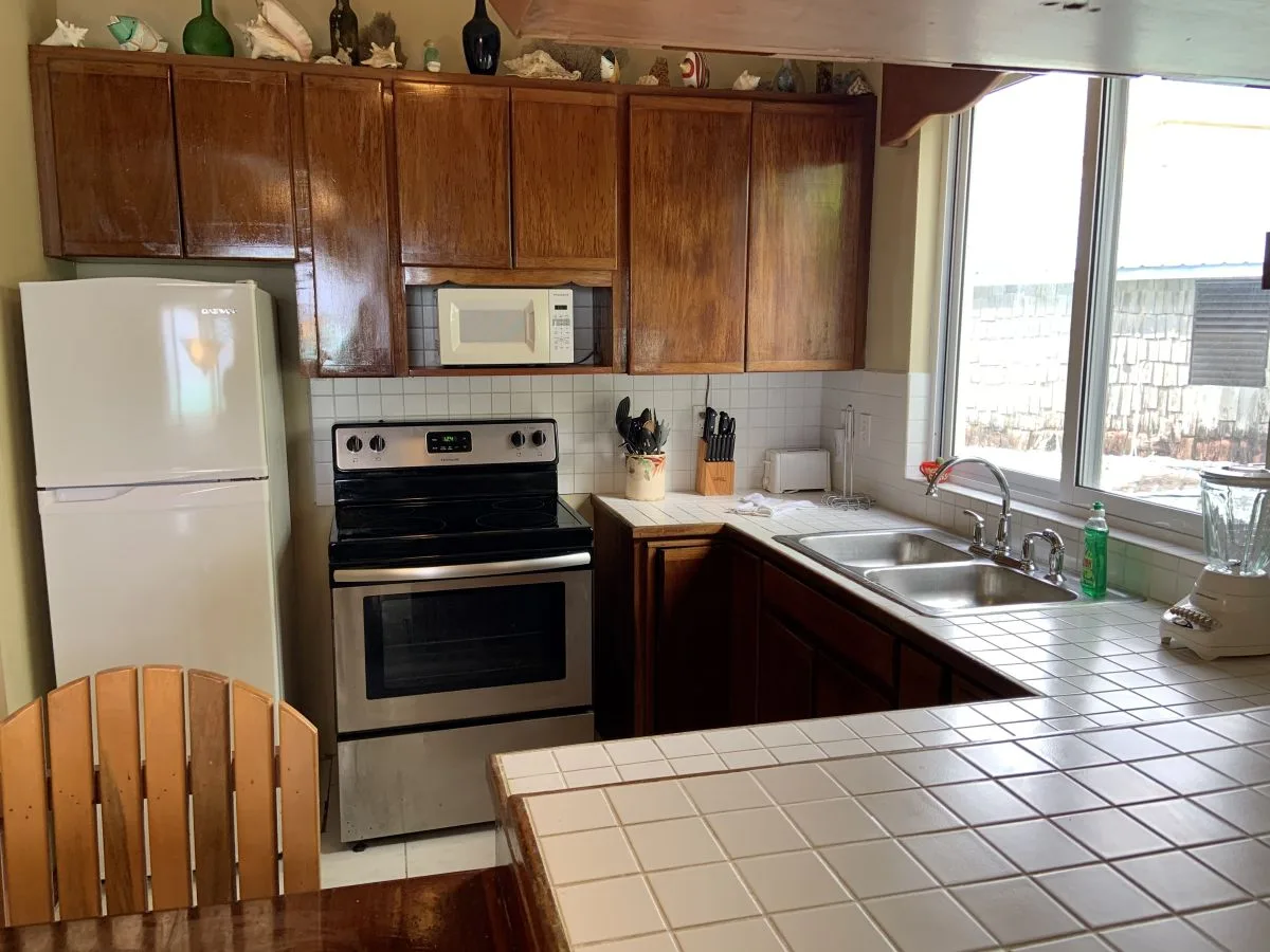 Una cocina con gabinetes de madera, una estufa y una encimera de azulejos junto a una ventana.