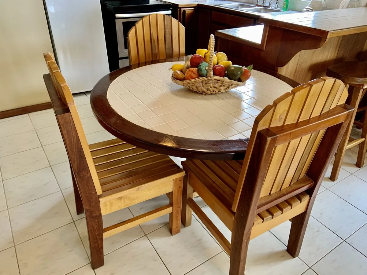 Una mesa redonda con asientos de madera y una cesta de fruta está en una cocina.
