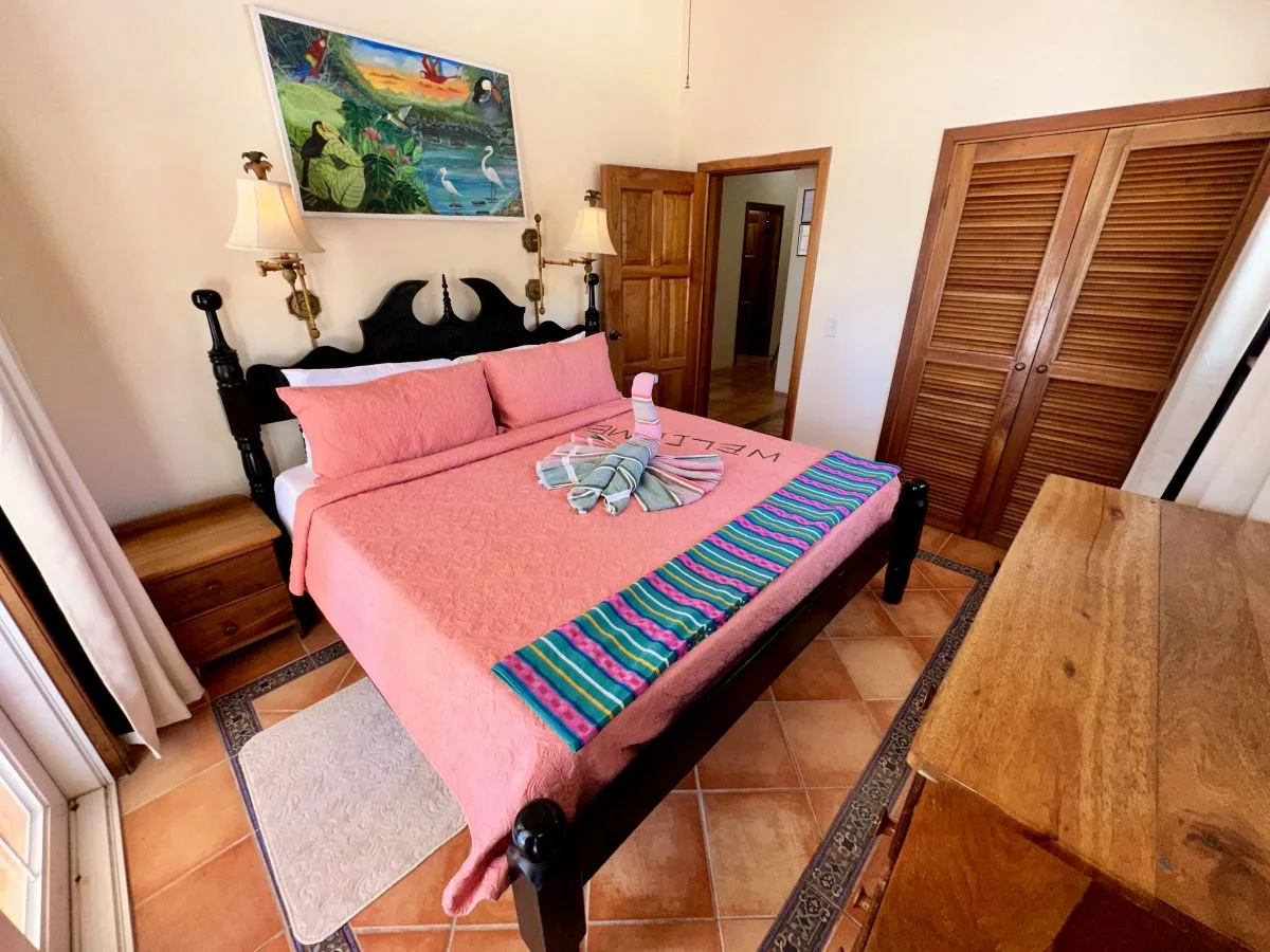 A bedroom with a pink bed, colorful runner, and wooden wardrobe.