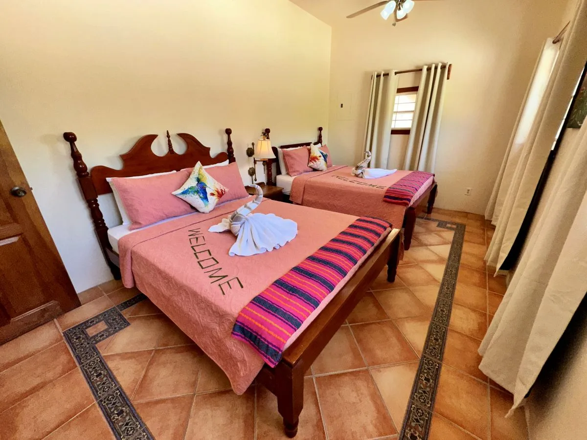 A bedroom with two beds dressed in pink bedding and colorful striped runners.
