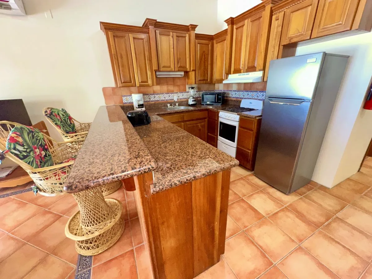 A kitchen with wooden cabinets, a stone countertop, and a refrigerator.